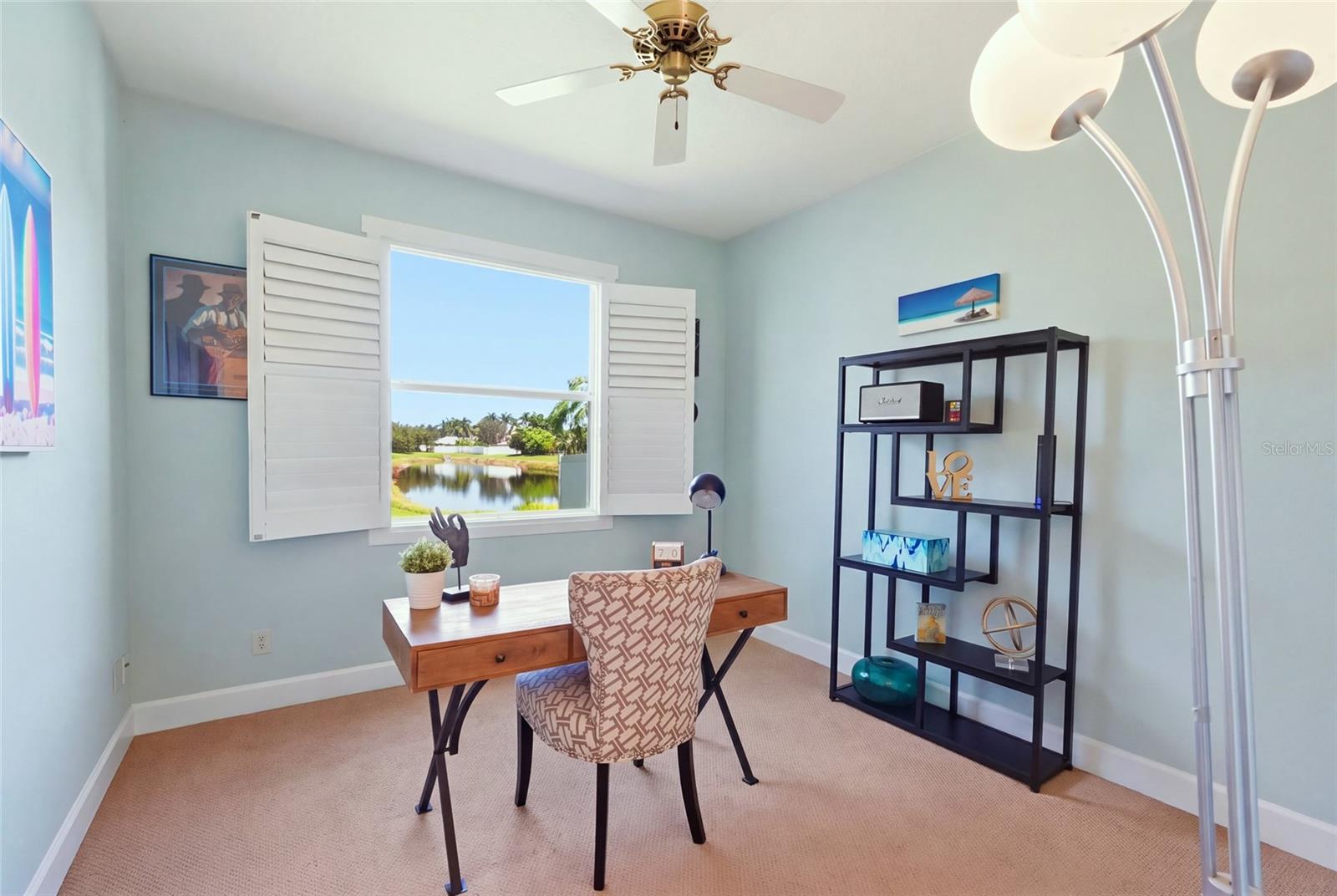 Furnished home office with a wooden desk and chair, plantation shutters, and a pond view.