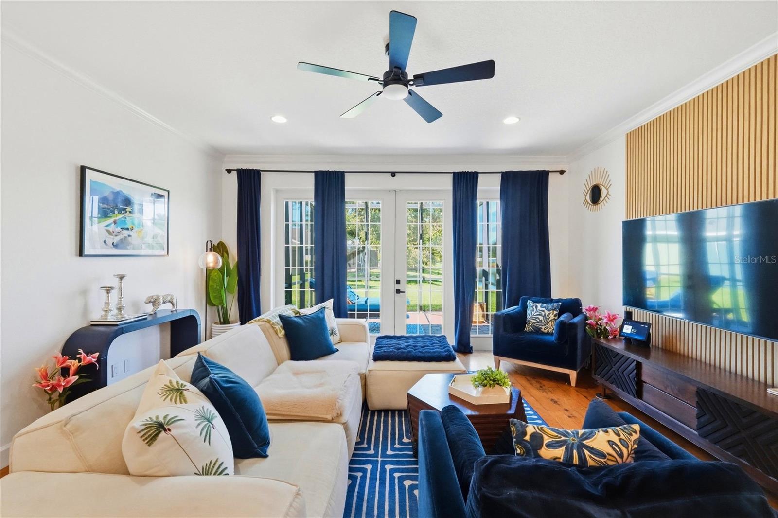 Living room with a cream sectional, navy chairs, and French doors opening to a sunny outdoor area.