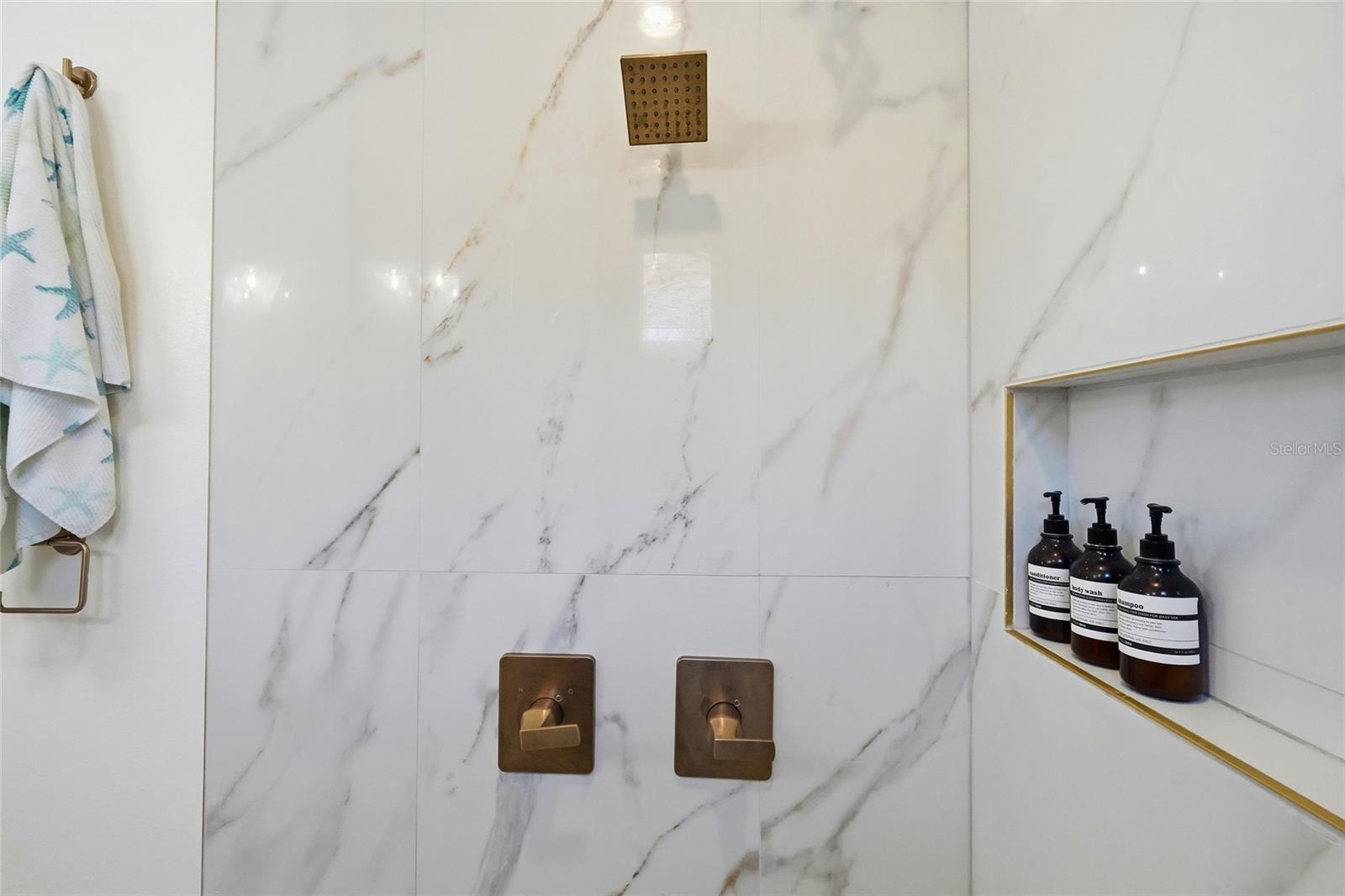 Marble-tiled shower with bronze fixtures and a gold-trimmed niche holding toiletries.