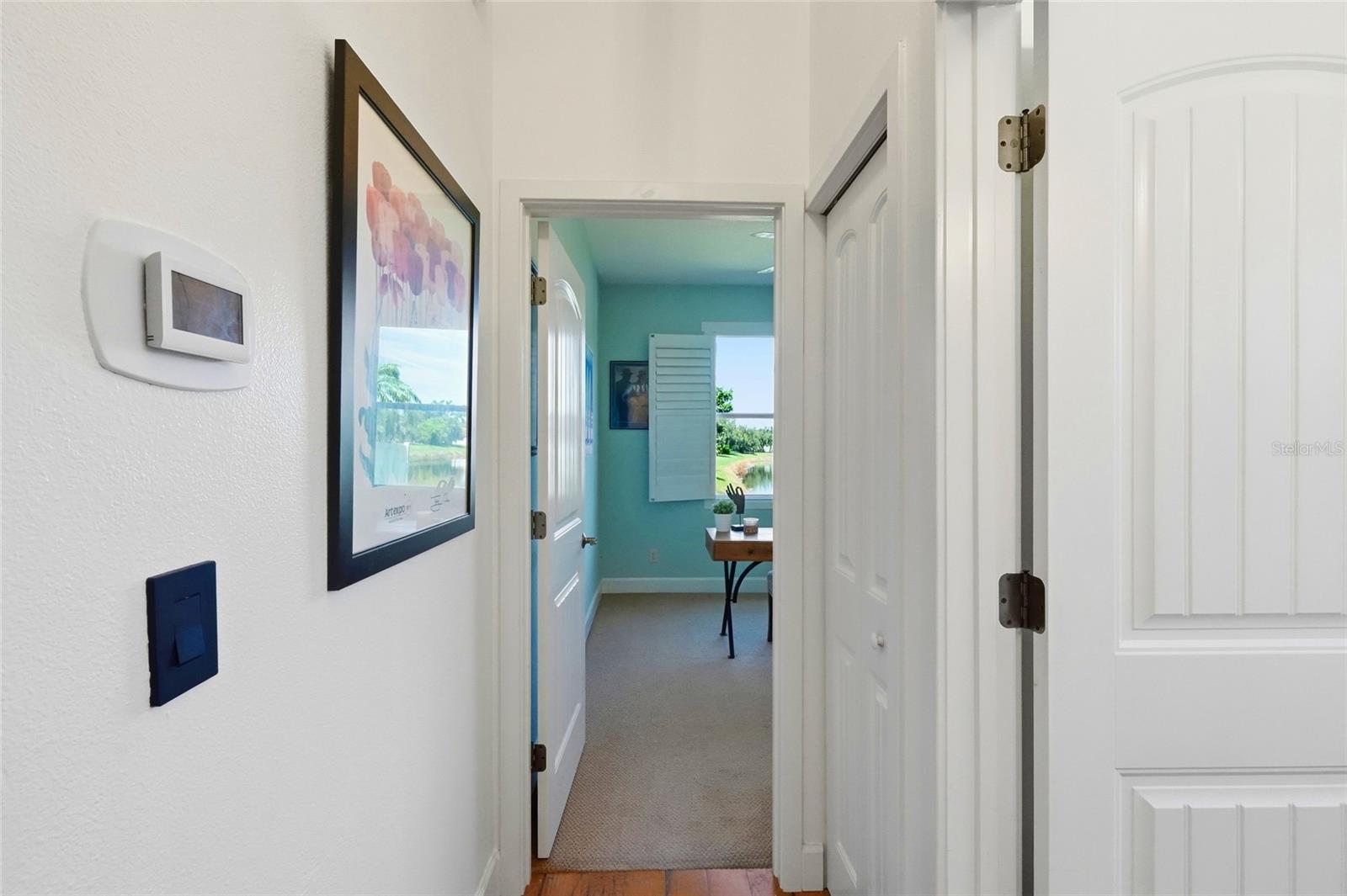 Hallway leading to a turquoise room with a desk and window overlooking water.