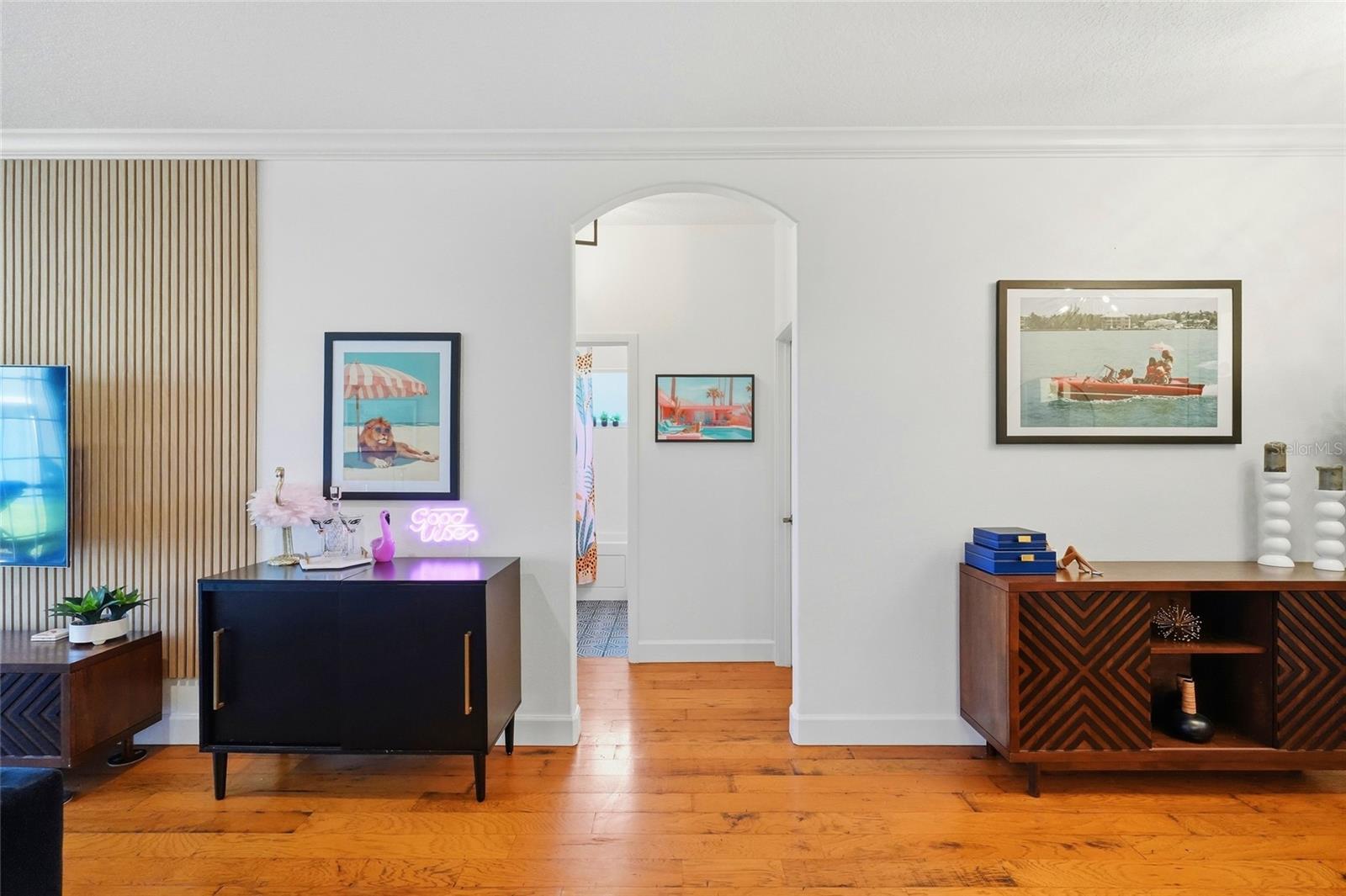 Furnished living room with warm wood floors, a slatted accent wall, and an arched doorway.