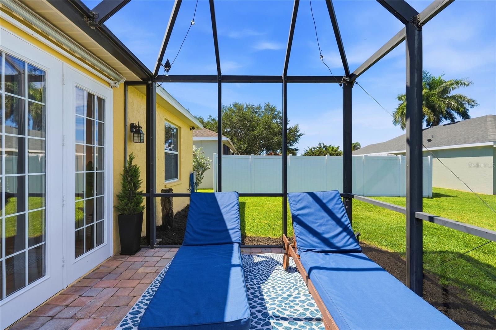 Screened patio with blue chaise lounges, brick pavers, and a fenced lawn.