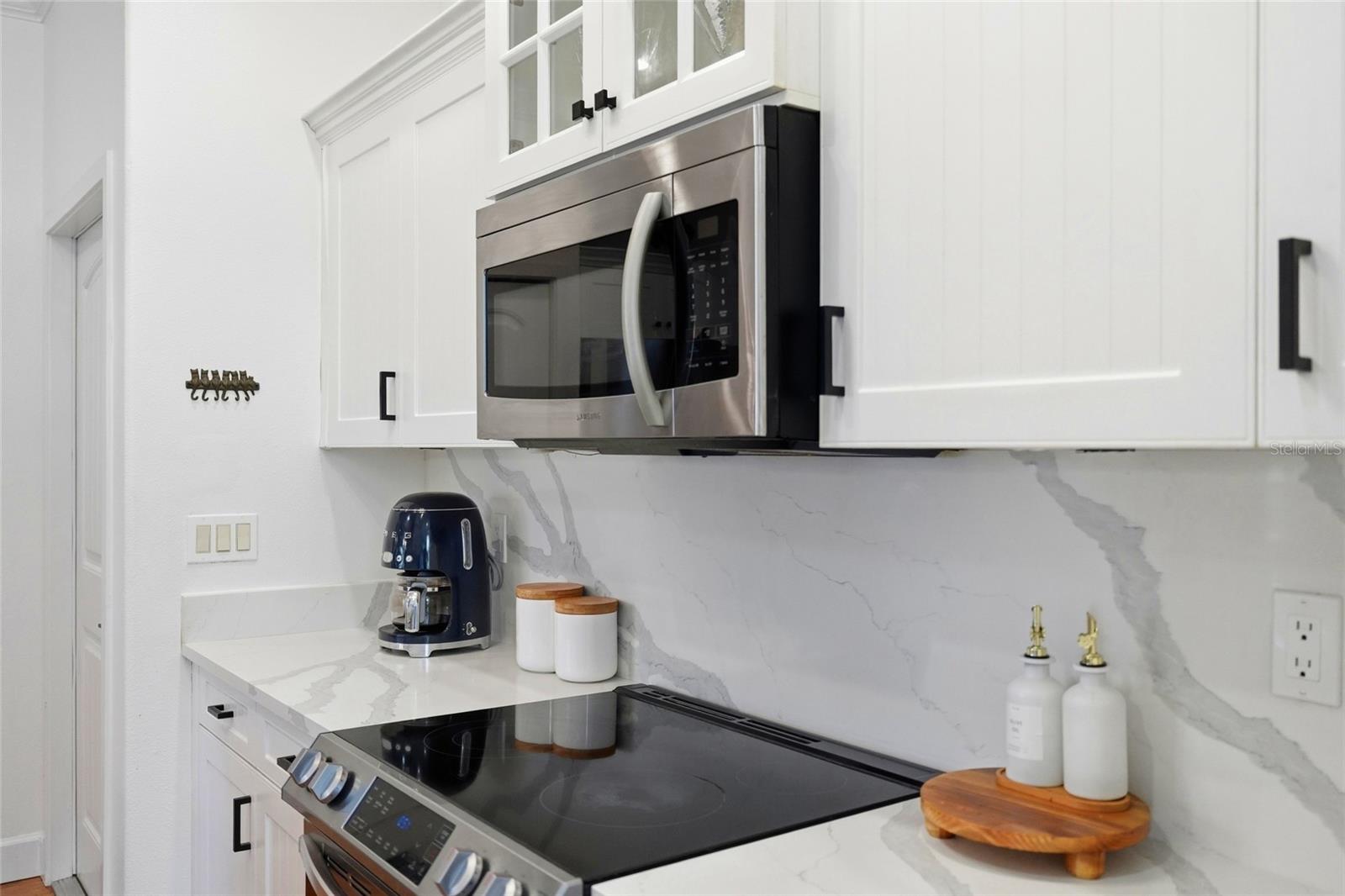 Kitchen with white cabinets, veined stone surfaces, and stainless steel appliances.