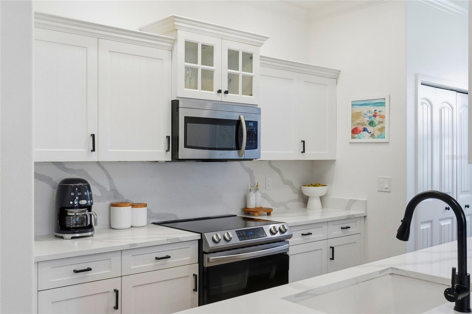 Kitchen with white cabinetry, veined stone backsplash, stainless appliances, and a black island faucet.