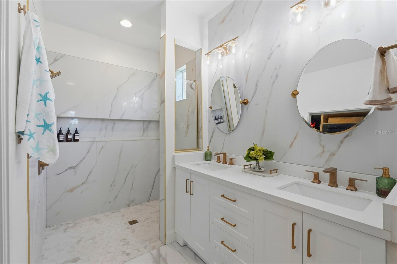 Bathroom with a marble-look walk-in shower and double vanity with brass fixtures.