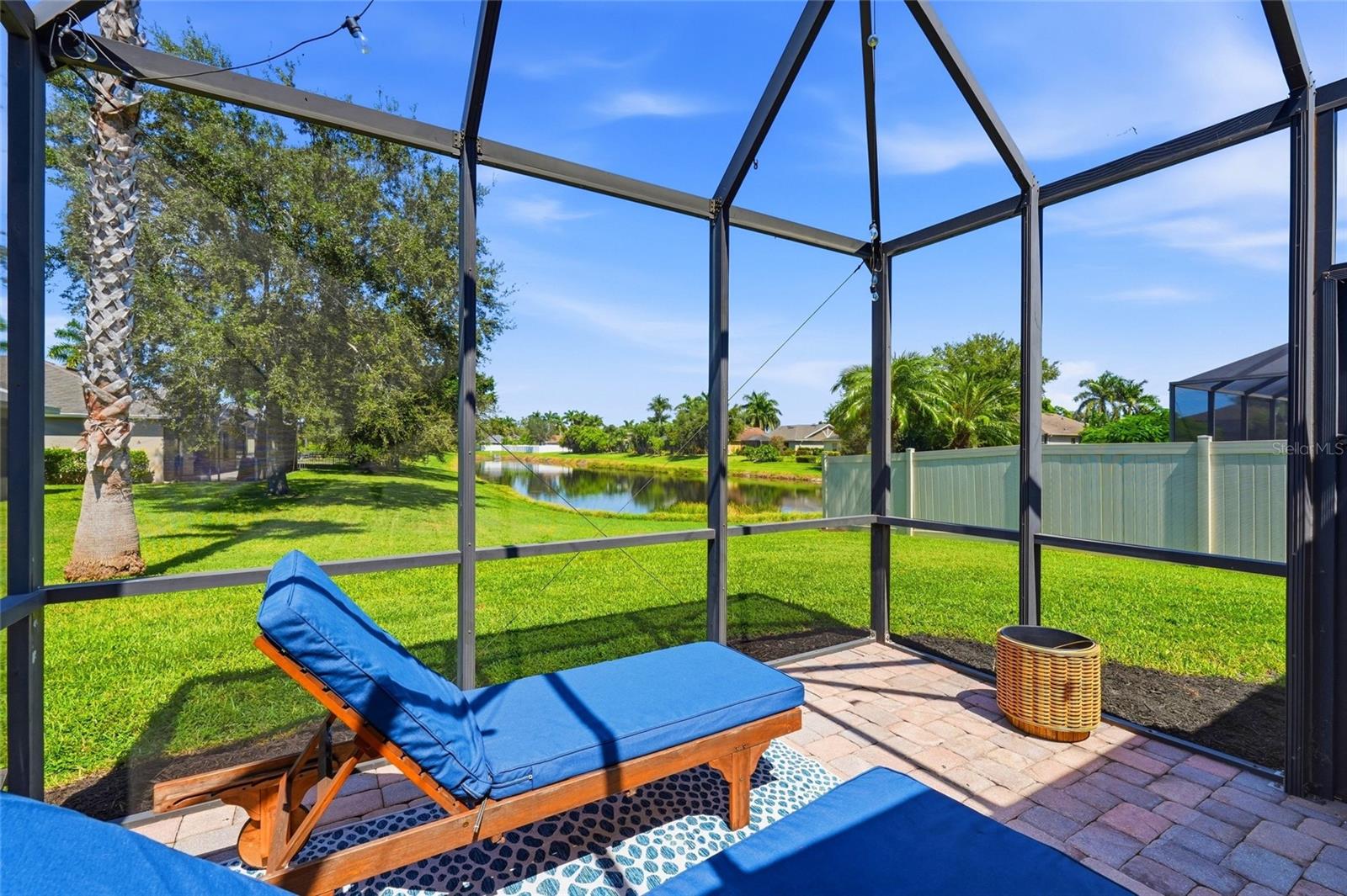 Screened patio with blue lounge chairs overlooking a pond and landscaped yard.