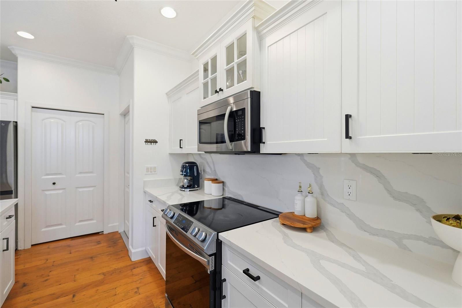 Bright white kitchen with marble-look counters, stainless steel appliances, and warm wood floors.