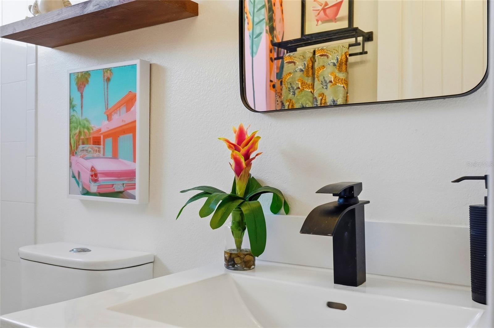 Bathroom vanity with a white sink, black faucet, orchid, and colorful framed artwork.