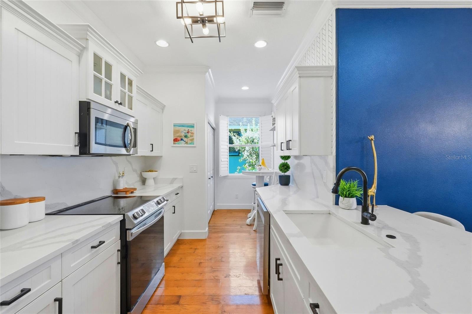 Bright galley kitchen with white cabinetry, marble-look counters, and a vivid blue accent wall.