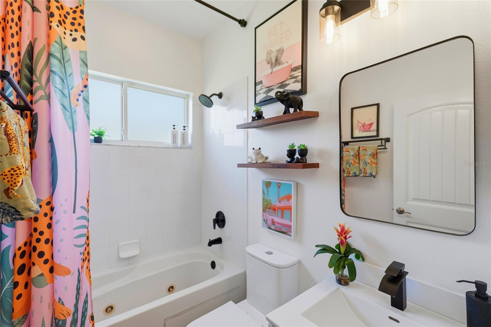 Bright bathroom with a white bathtub, colorful patterned shower curtain, and large rounded mirror.