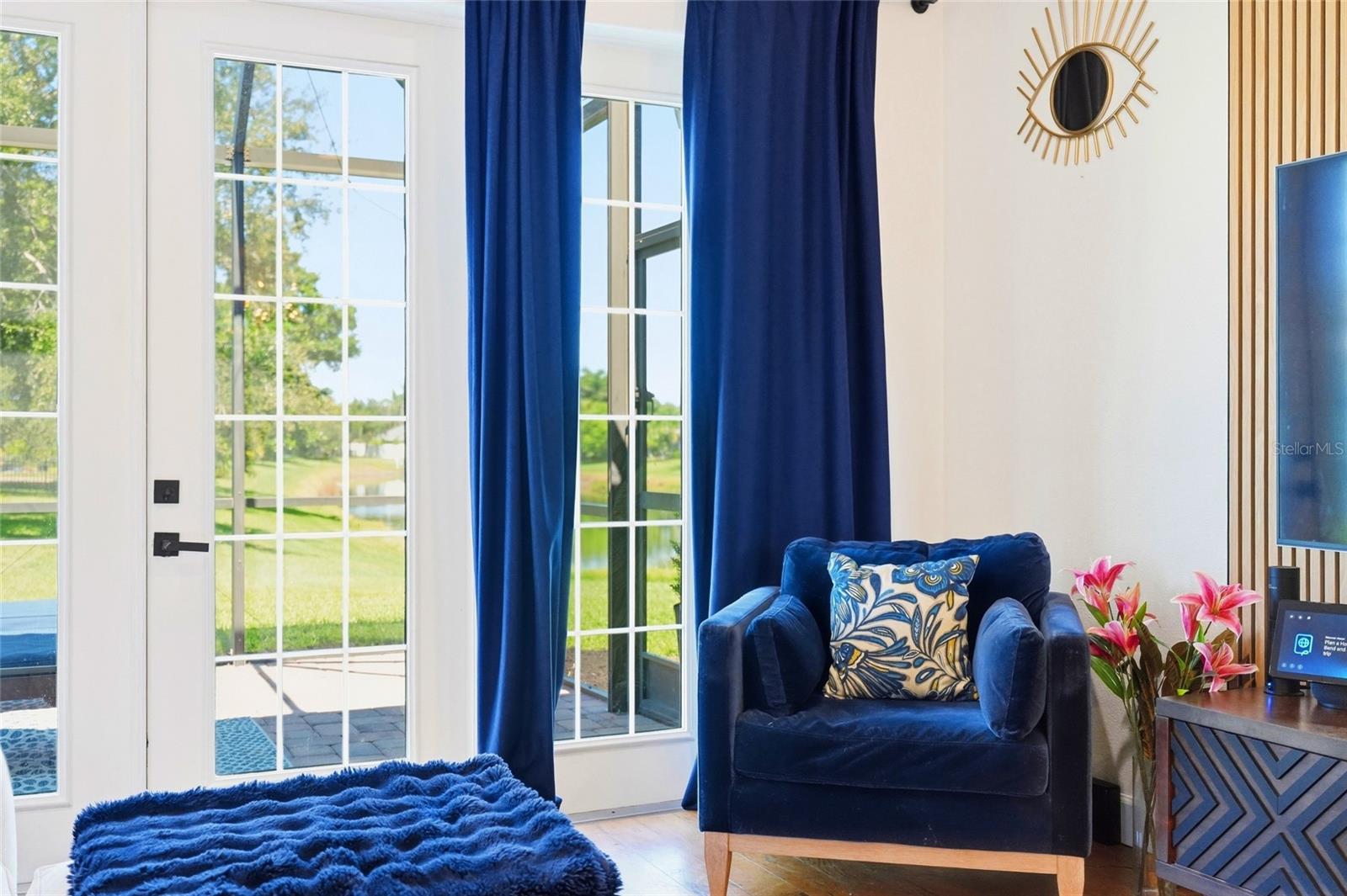 Living room with a navy velvet armchair beside tall windows overlooking a green lawn.