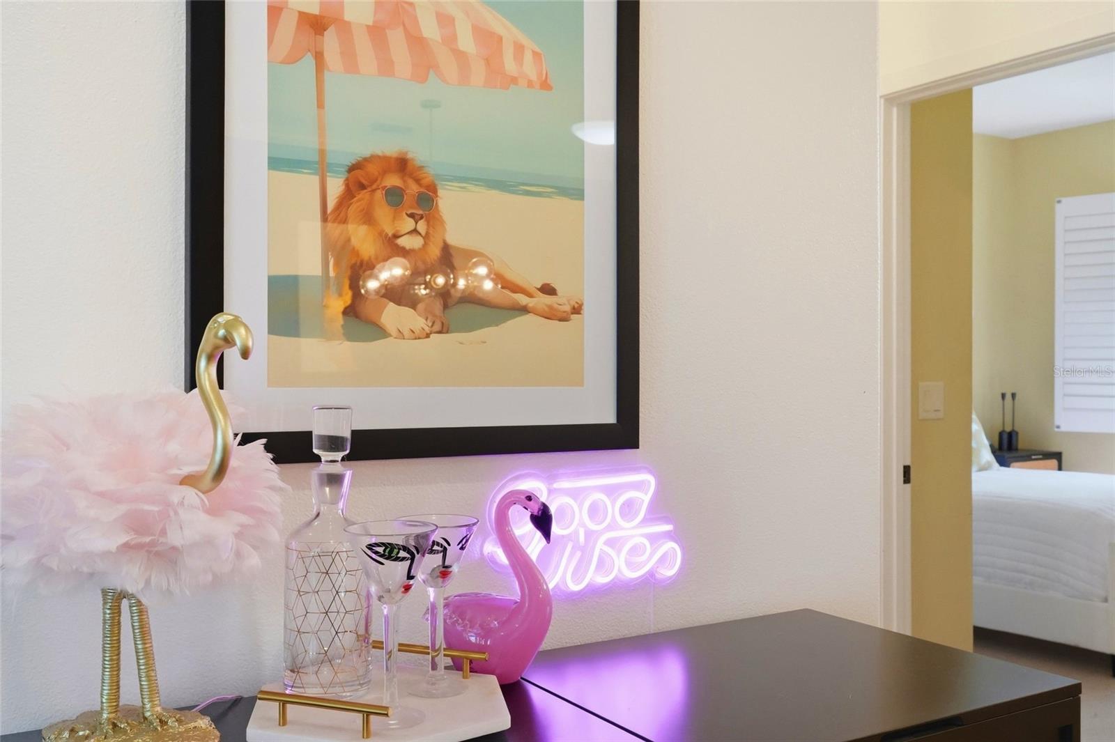 Bedroom dresser with pink flamingo decor, a glowing “Good Vibes” sign, and framed beach-themed lion art.