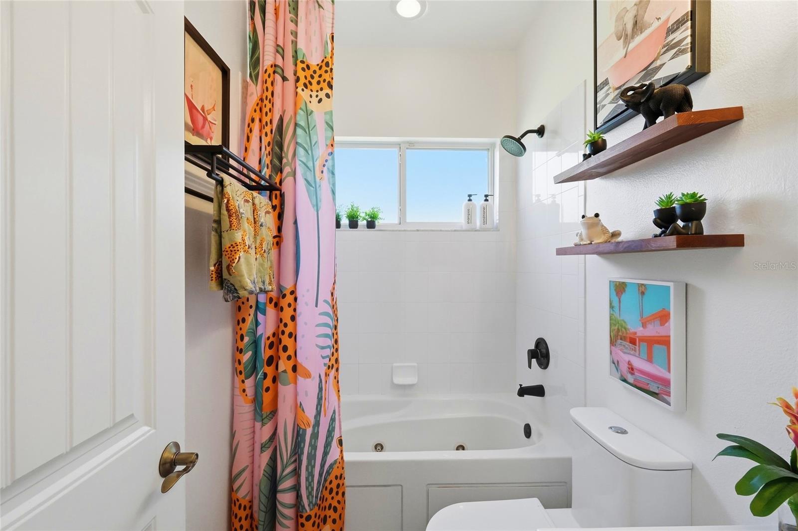Bathroom with a jetted tub, colorful patterned shower curtain, and window above the tub.