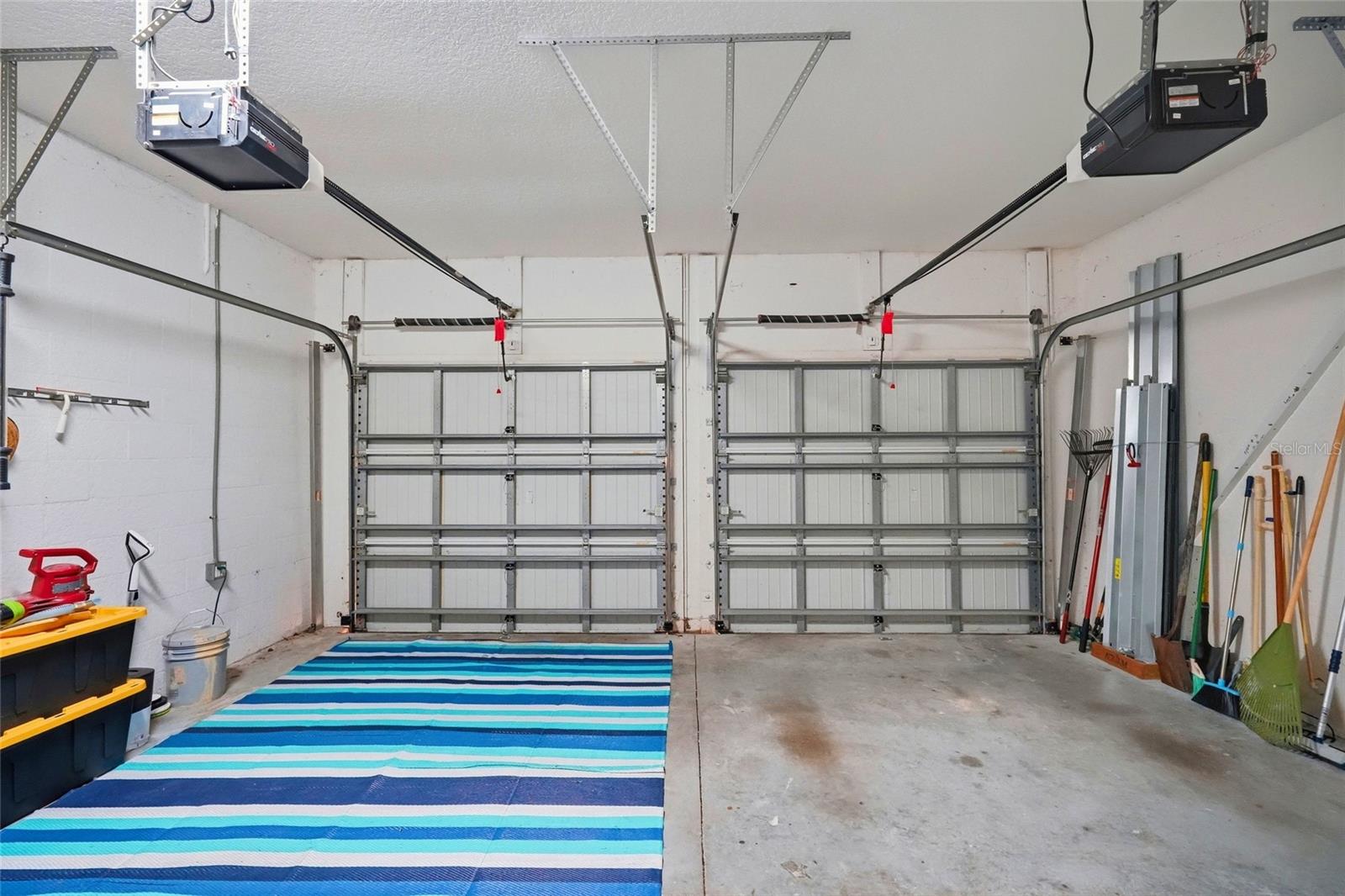 Two-car garage with closed doors, a blue striped floor mat, and tools along the walls.