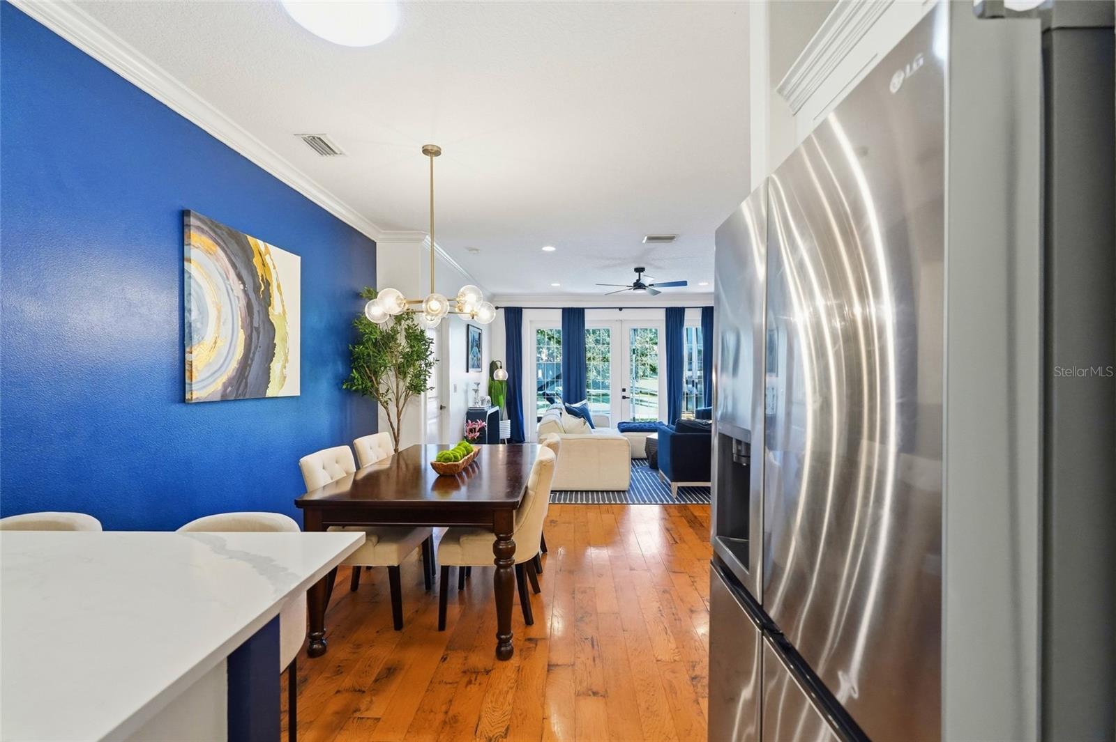 Open-plan kitchen and dining area with a blue accent wall, stainless steel refrigerator, and hardwood floors.