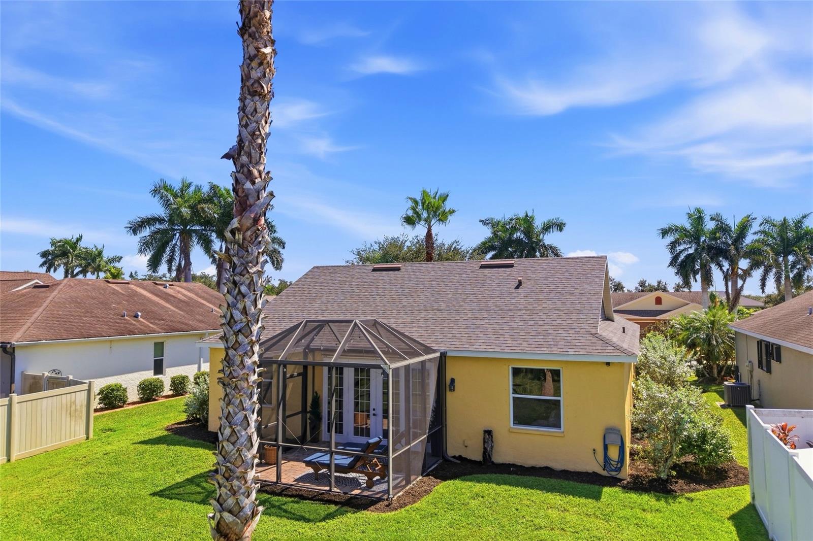 Yellow house with a screened lanai, outdoor seating, green lawn, and tall palm trees.