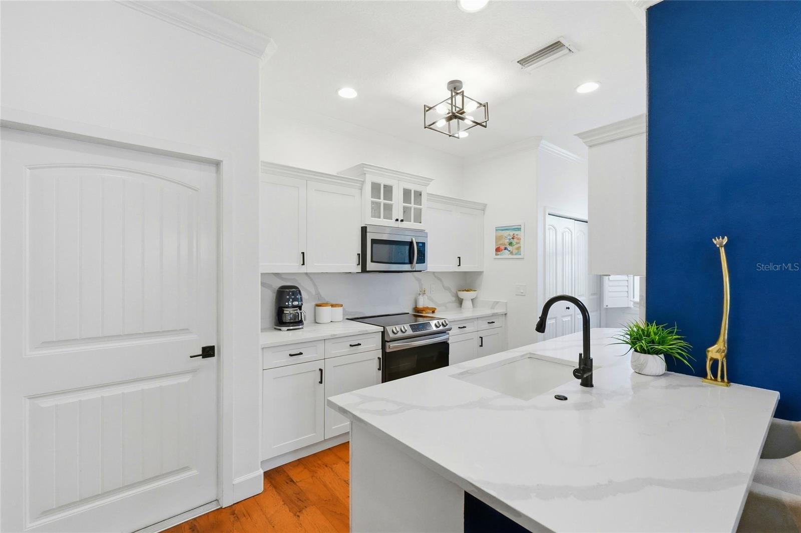 White kitchen with a large marble-look island, black faucet, stainless appliances, and blue accent wall.