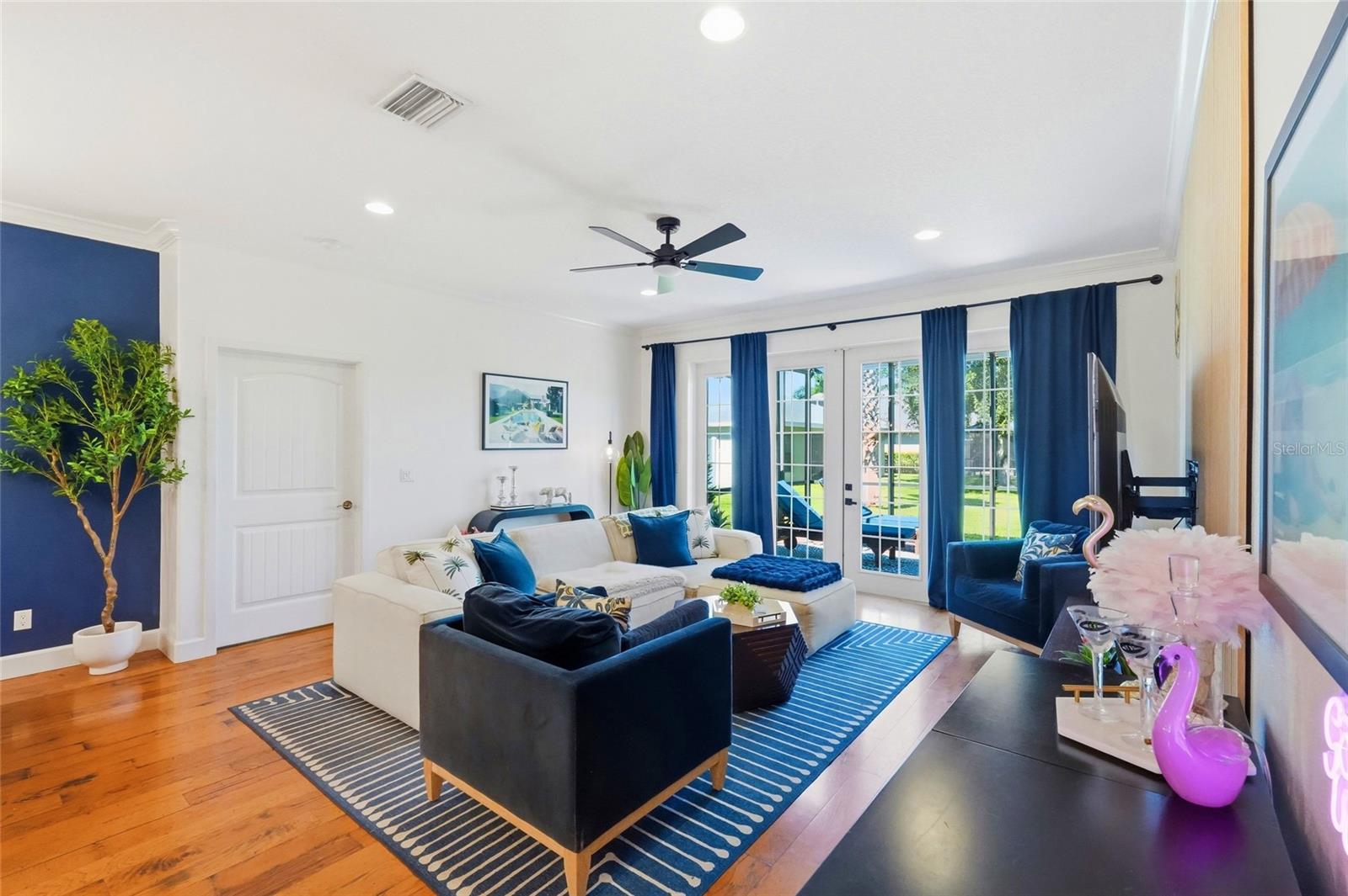 Living room with a white sectional, navy chairs, striped rugs, and blue-curtained doors to the yard.