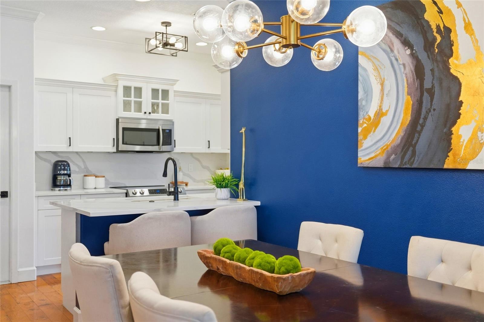 Kitchen and dining area with white cabinetry, a marble-look island, and a vivid blue accent wall.