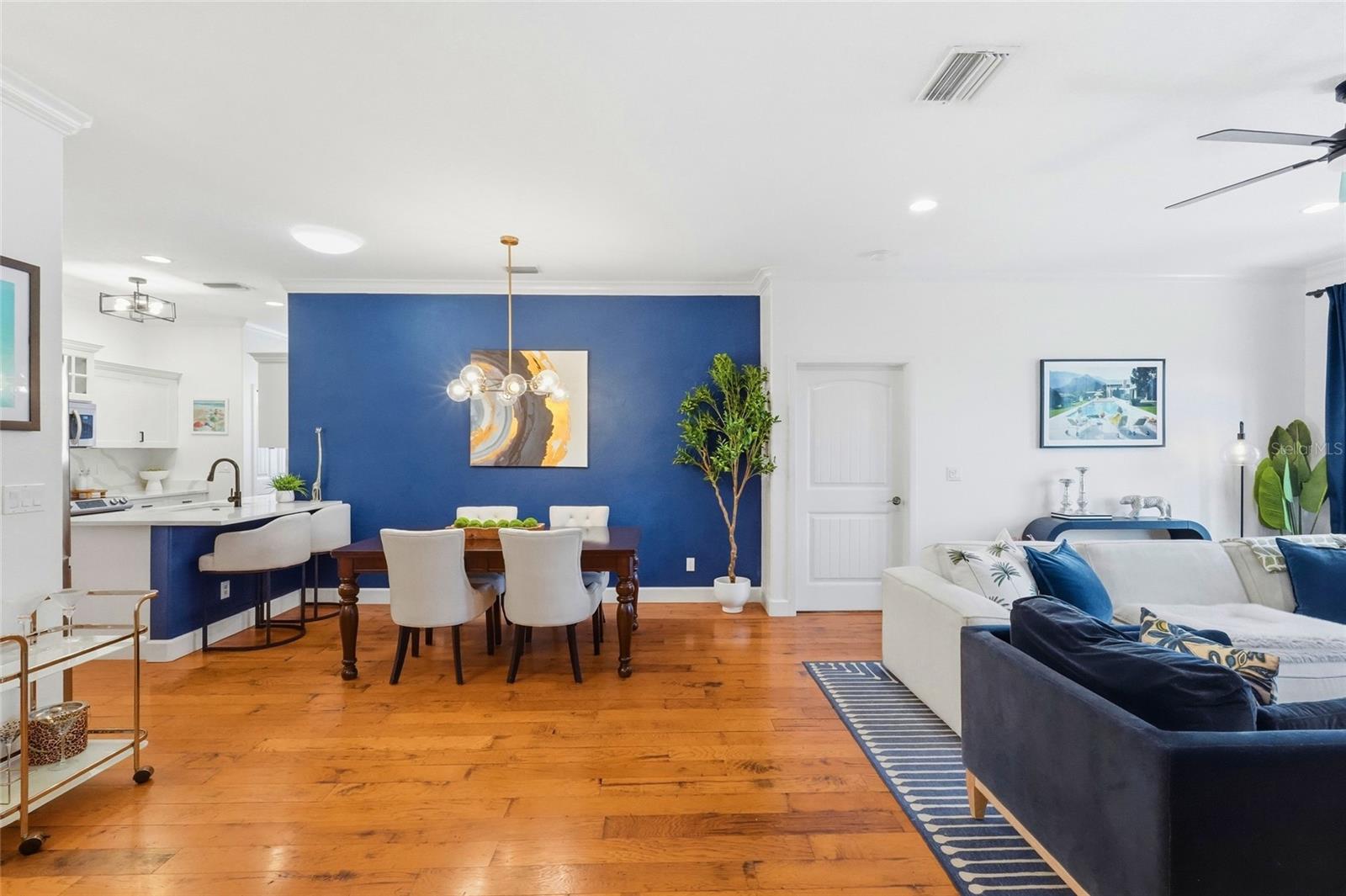 Open-plan living and dining area with a blue accent wall, wood floors, and a white sofa.
