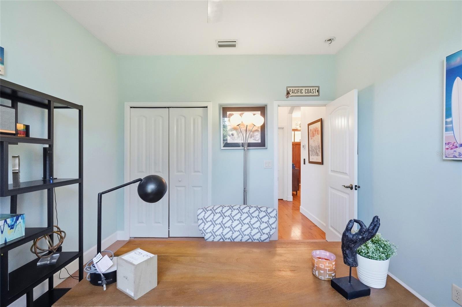 Furnished room with pale blue walls, wood floors, white closet doors, and an open doorway.