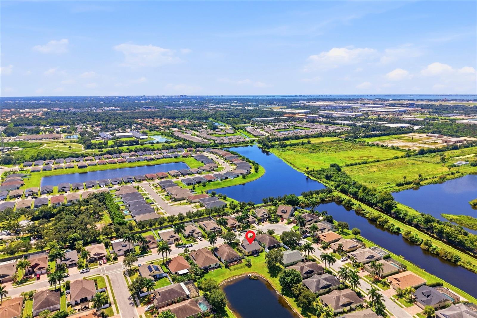 Aerial view of a suburban home marked by a red pin, beside winding ponds and green space.
