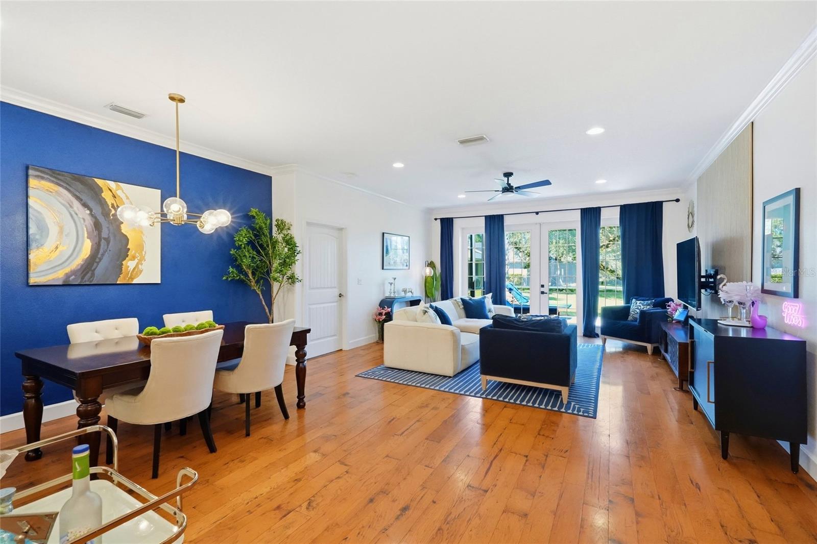 Open living and dining room with wood floors, a blue accent wall, and French doors to the yard.