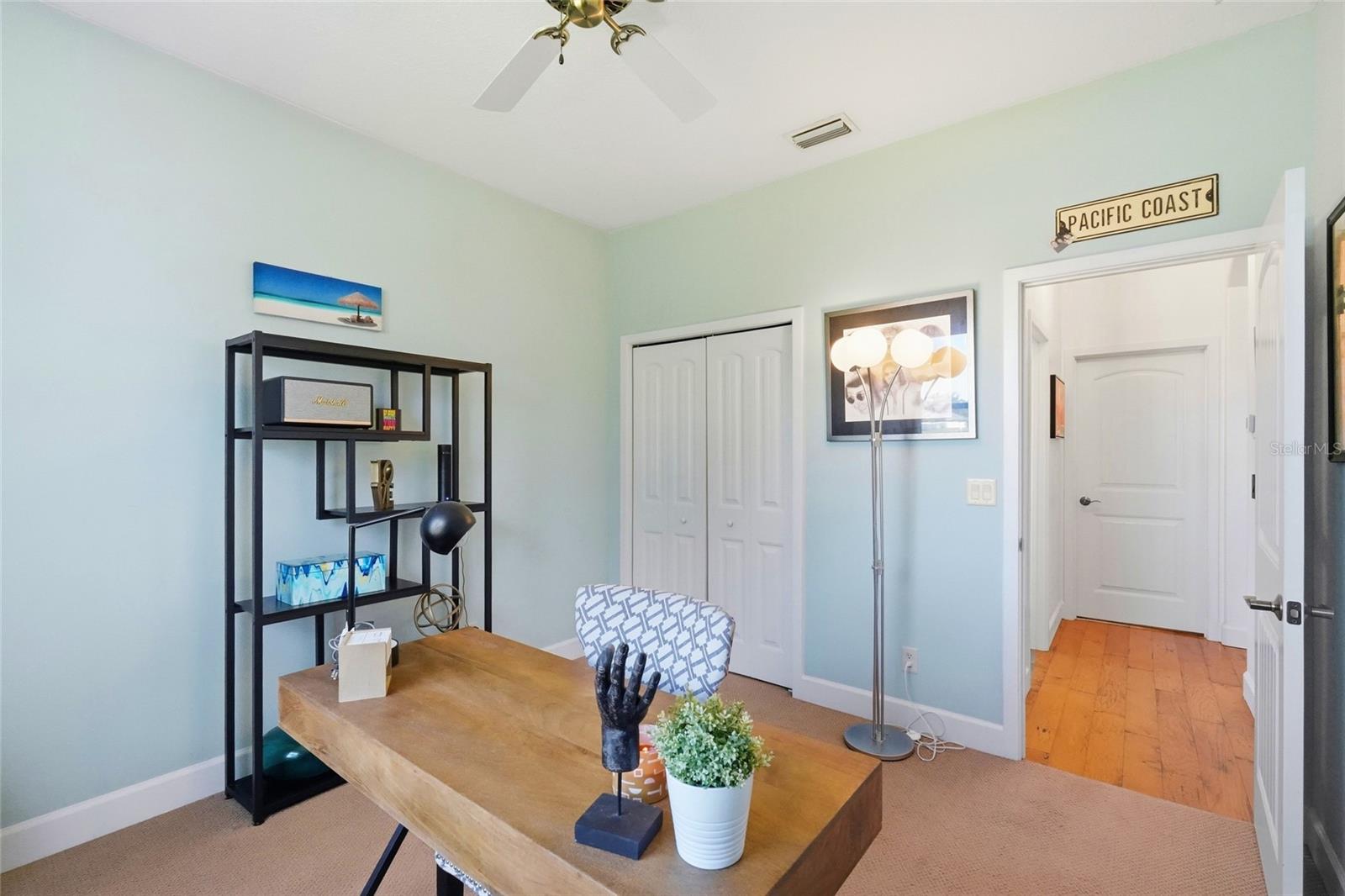 Furnished home office with a wooden desk, black shelving, and pale blue walls.