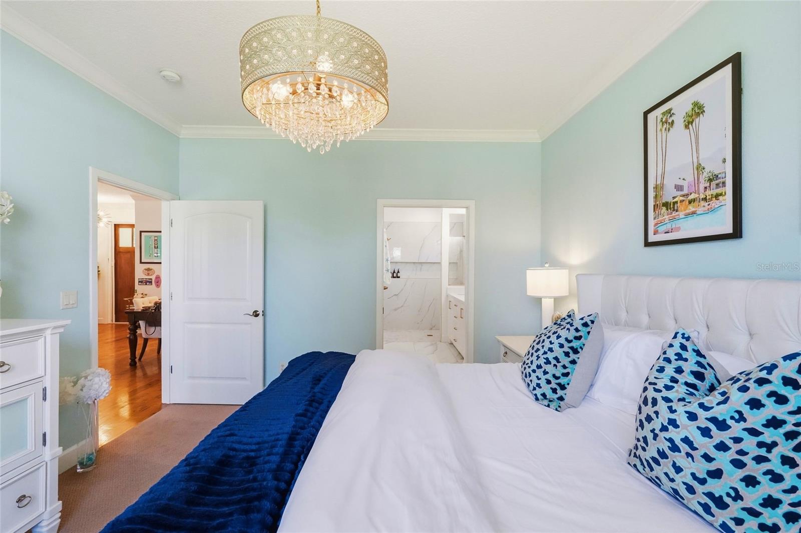 Bedroom with pale blue walls, white bedding, blue patterned pillows, and a crystal chandelier.