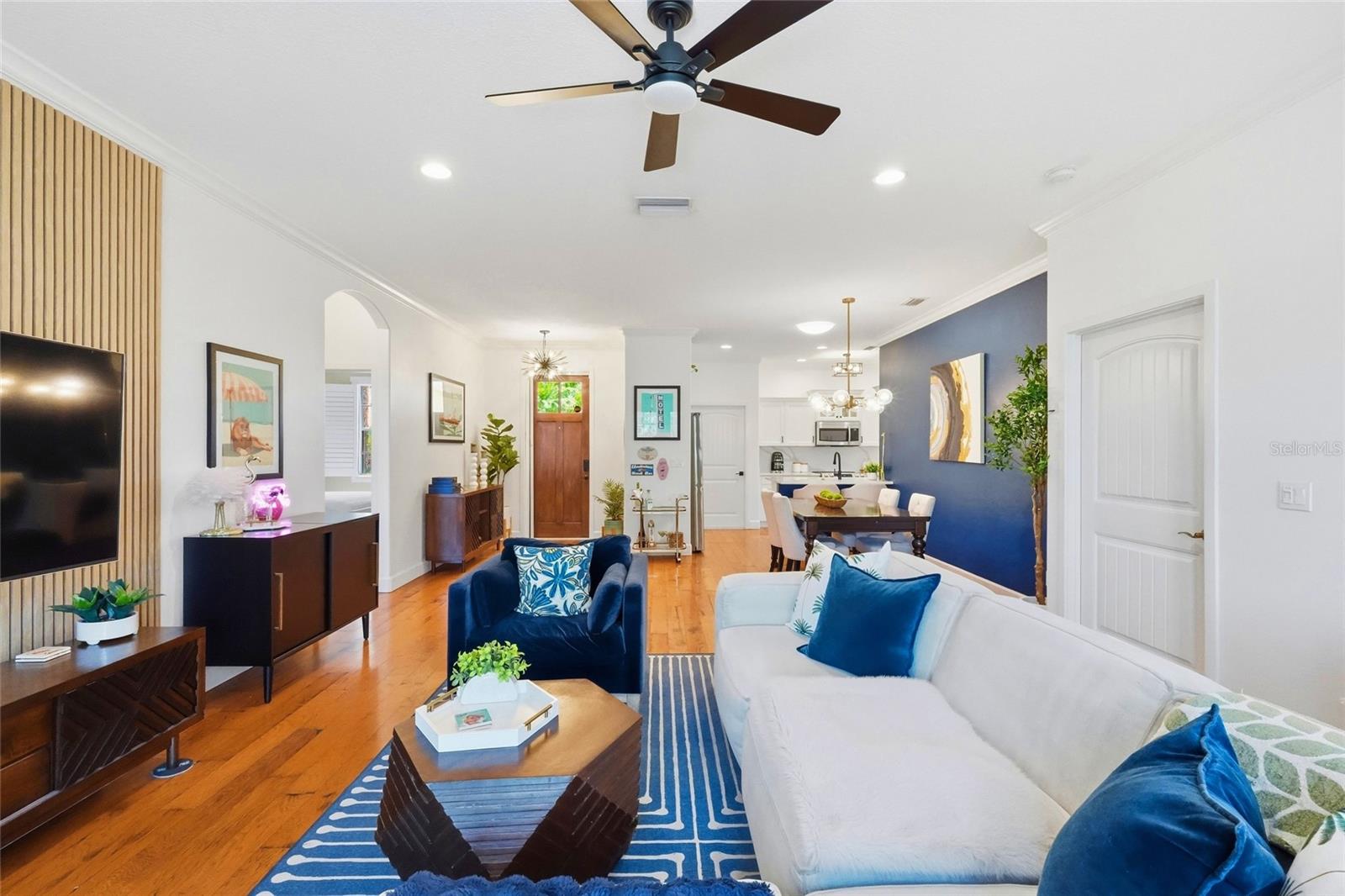 Open-plan living room with hardwood floors, white sofa, blue armchairs, and dining area beyond.