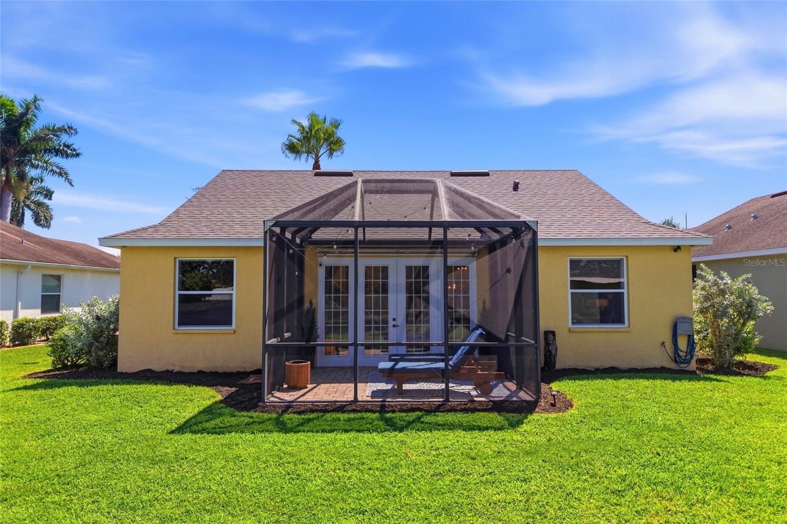 Yellow stucco home with a screened lanai and patio seating facing a broad green lawn.
