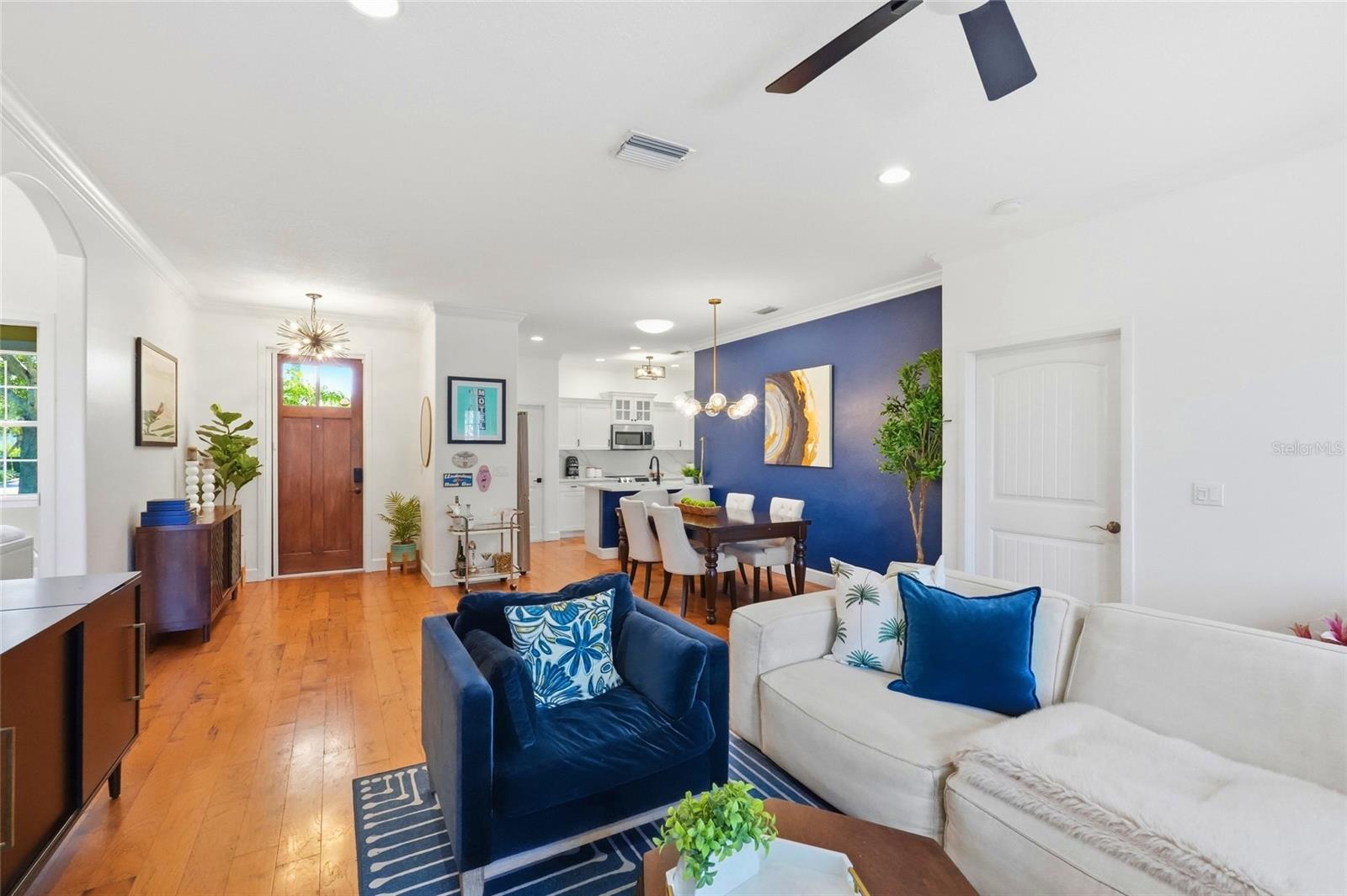 Open living and dining room with wood floors, a blue accent wall, and a white kitchen.