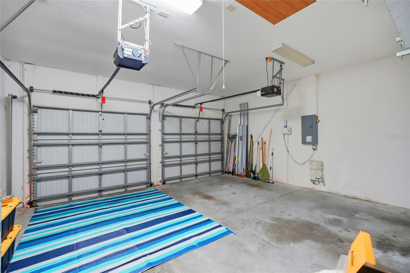 Two-car garage with closed overhead doors, a blue striped floor mat, and tools along the wall.