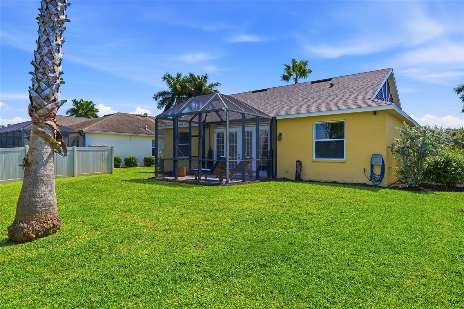 Yellow home with a screened lanai and spacious lawn, framed by a palm tree.