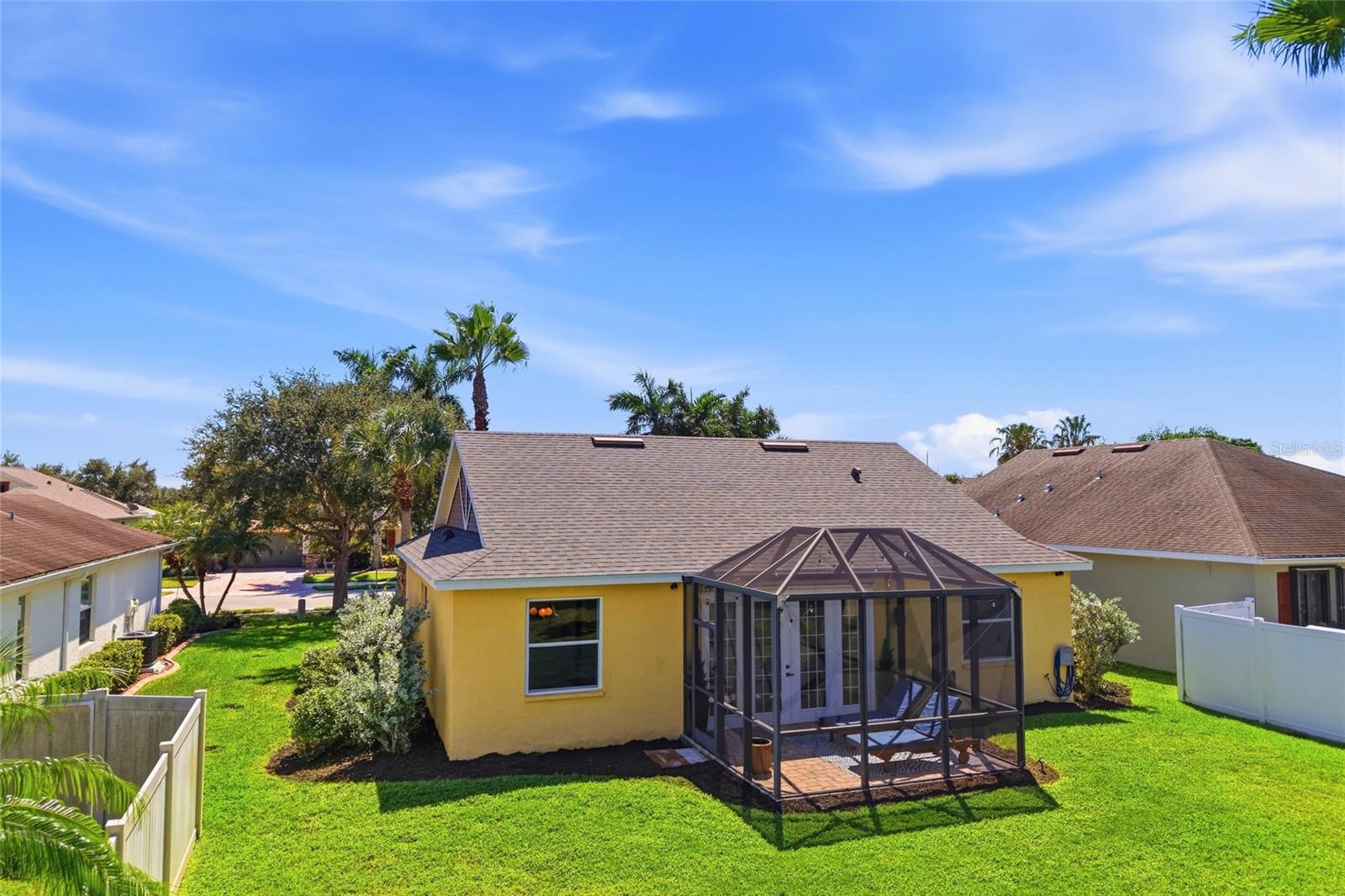 Yellow house with a screened lanai opening onto a broad lawn, with palm trees behind it.