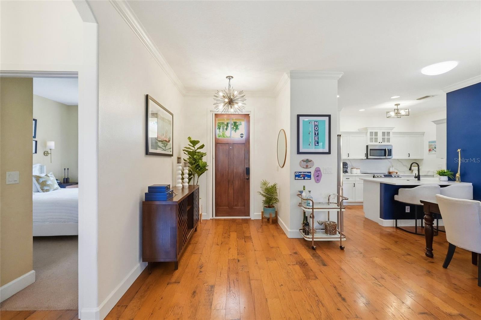 Entry foyer with wood flooring, a wood front door, and an open white-and-blue kitchen.