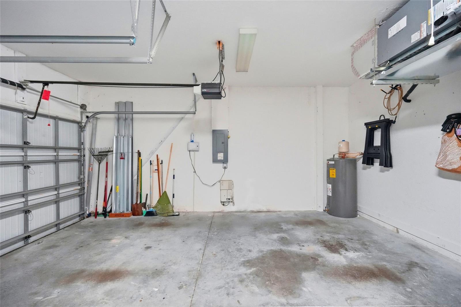 Garage with a concrete floor, overhead door, water heater, and yard tools along the walls.