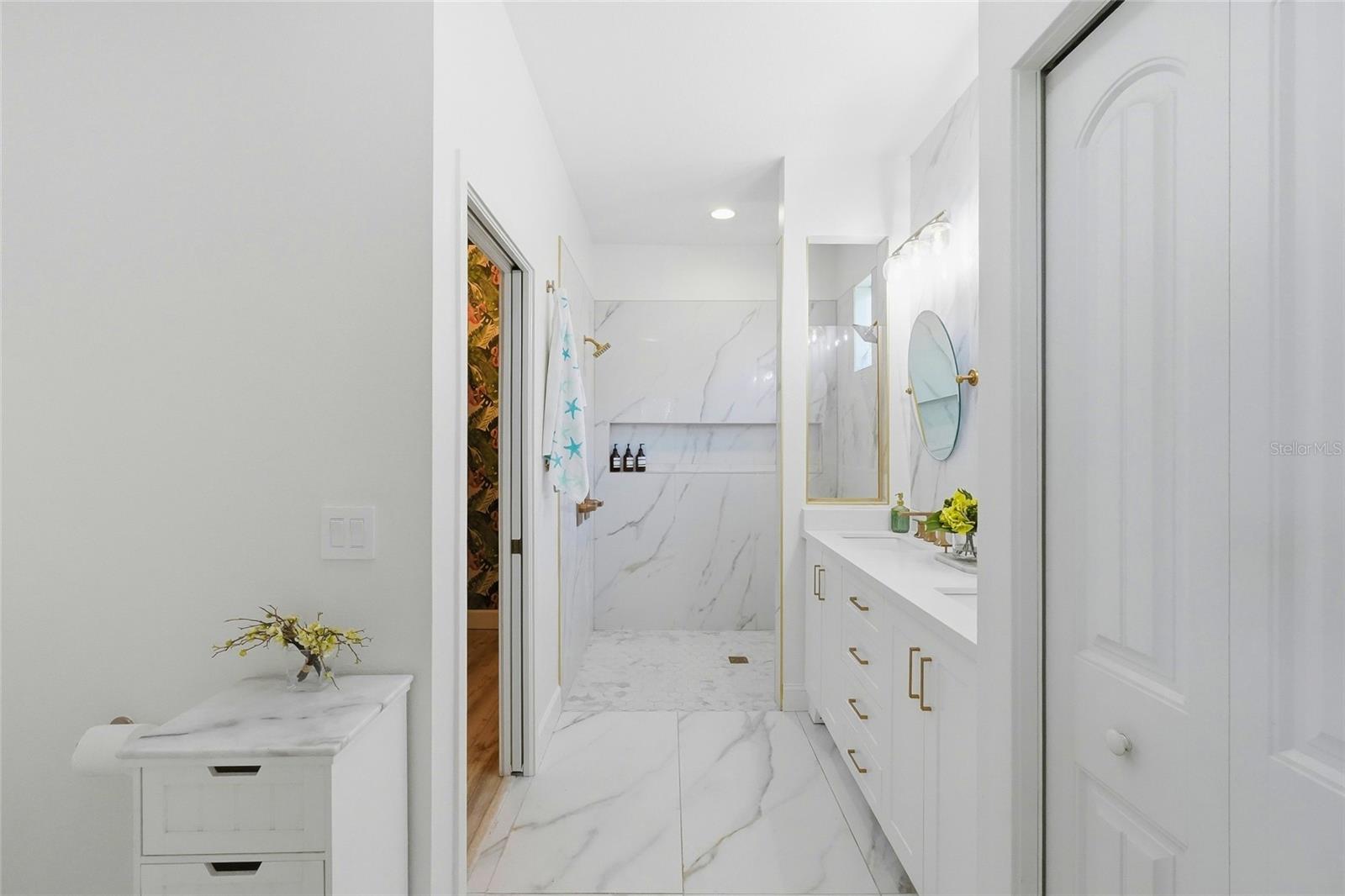 Bright bathroom with marble-look tile, a walk-in shower, and a white vanity with gold hardware.