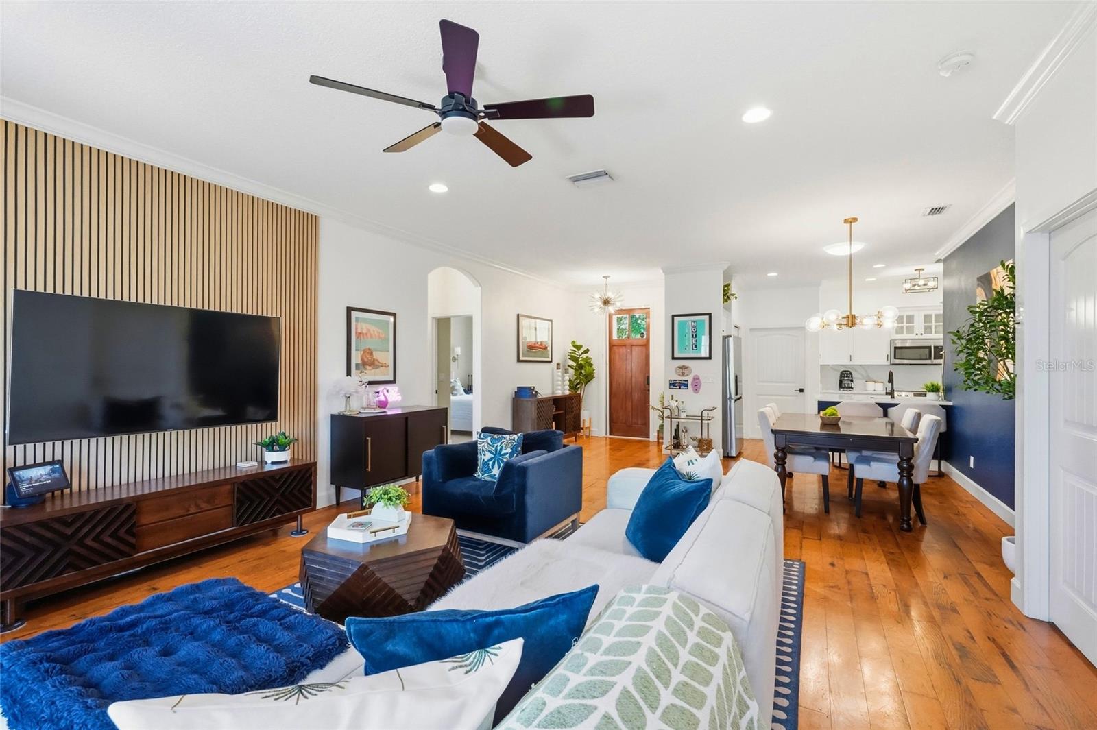 Open-plan living and dining room with blue-and-white seating, a slatted TV wall, and warm wood floors.