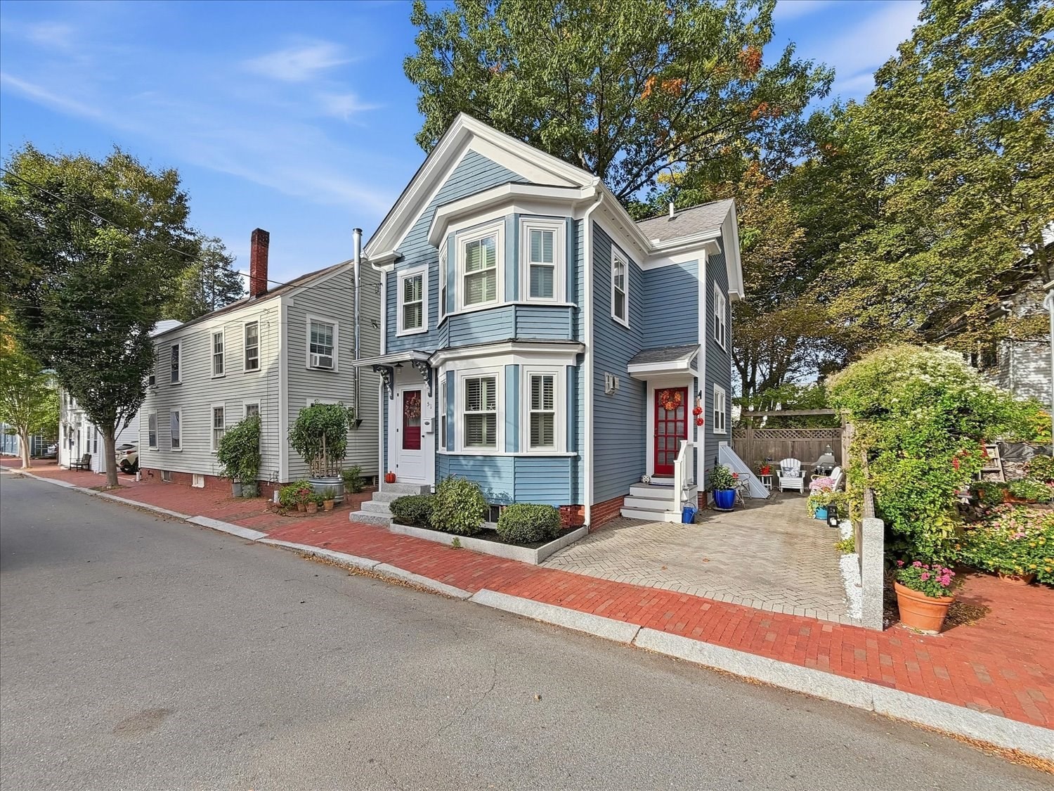 Blue clapboard house with bay windows, red doors, brick sidewalk, and a garden patio.
