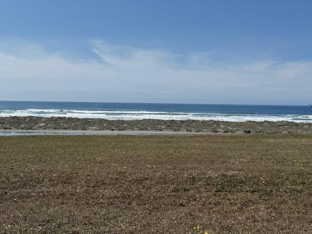 Grassy coastal lot overlooking a rocky shoreline and ocean waves.