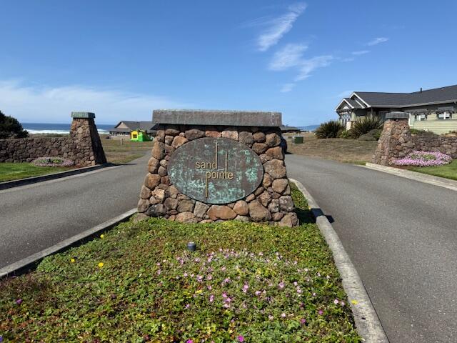 Sand Pointe stone entrance sign beside a curving road, with the ocean in the distance.