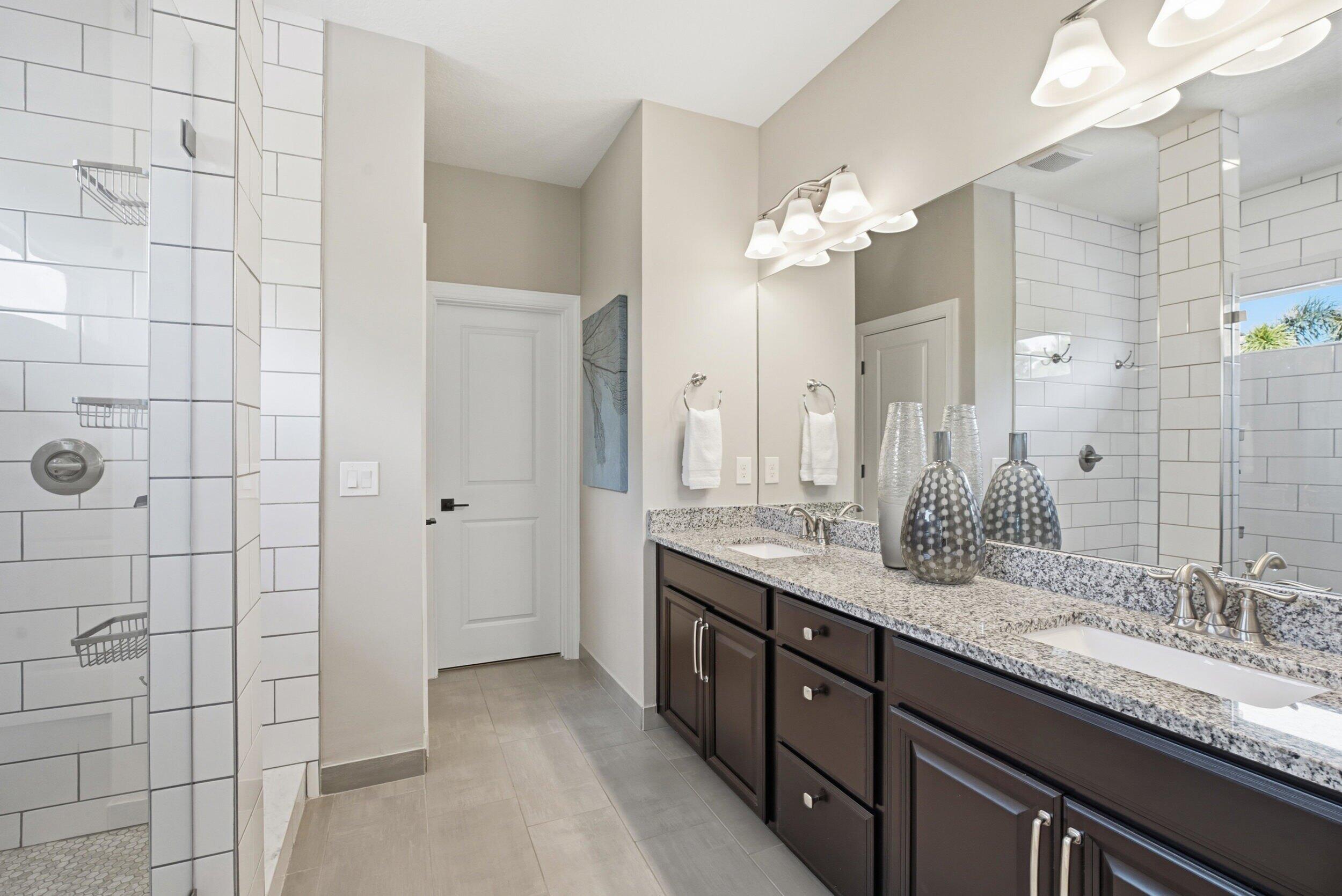 Bathroom with a double-sink granite vanity and a white subway-tile shower.
