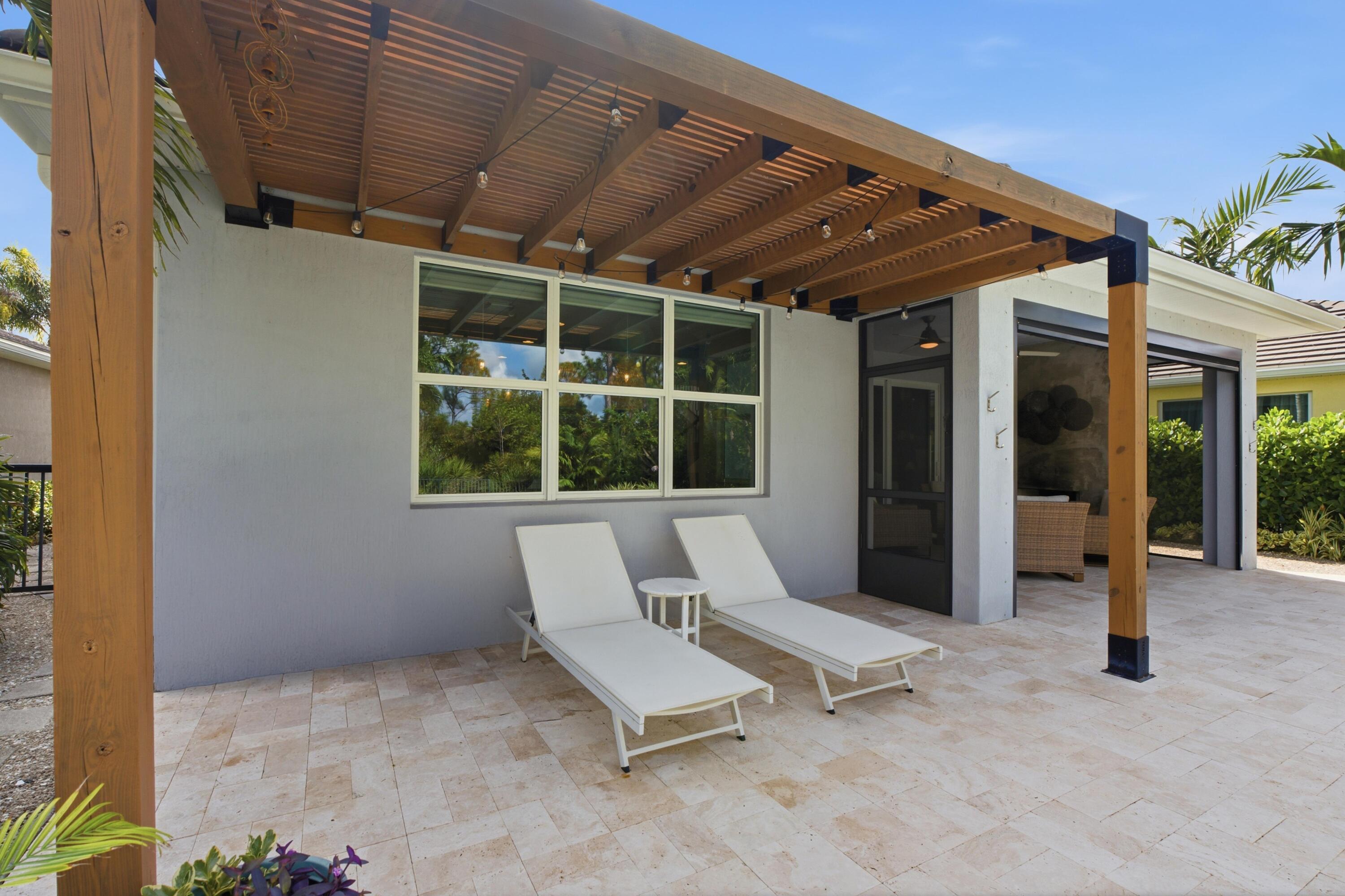 Tiled home patio with a wooden pergola, string lights, and two white chaise lounges.