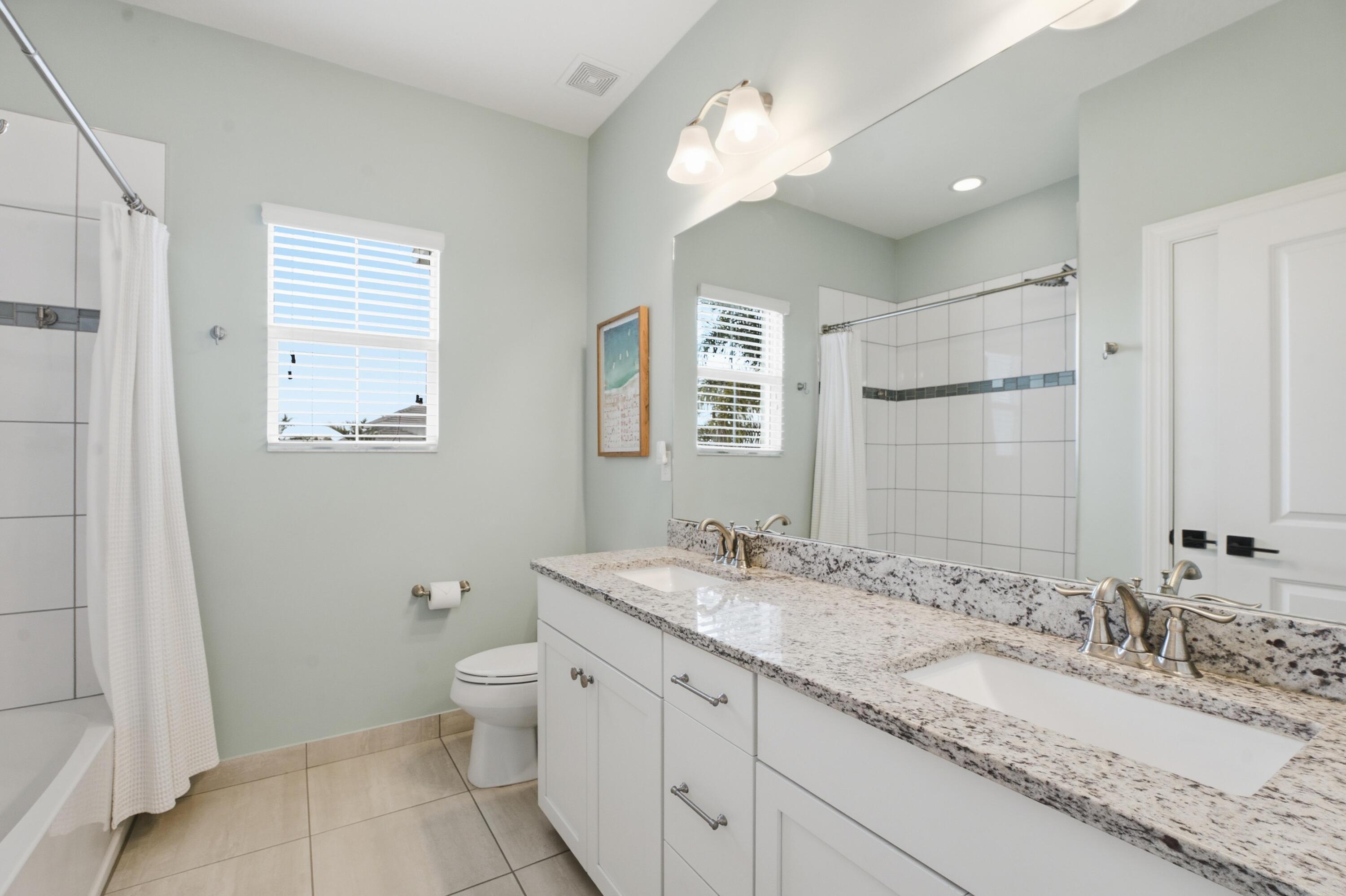 Bathroom with a granite double-sink vanity, large mirror, and tiled shower behind a white curtain.