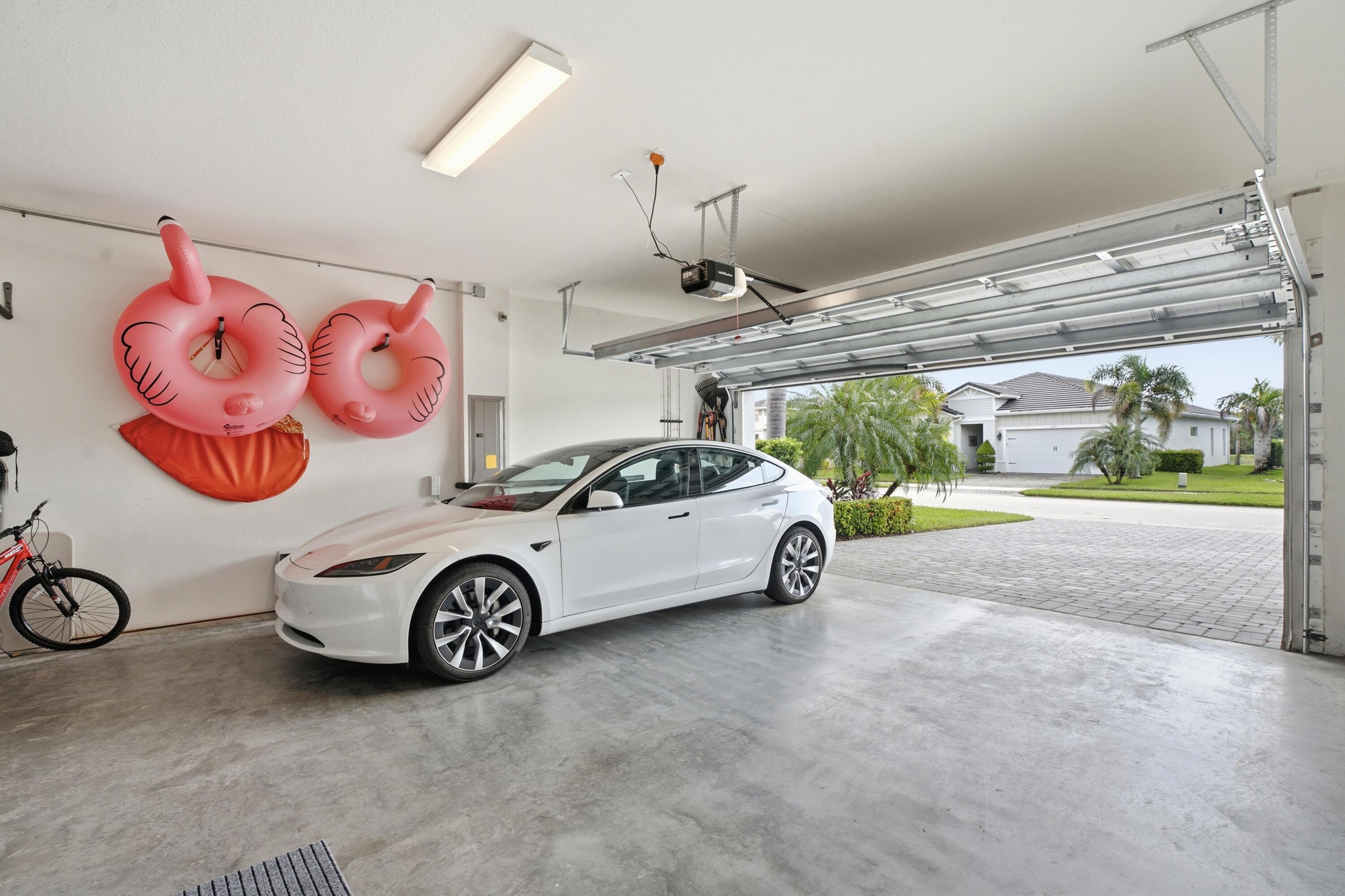 Garage with a white car, pink inflatable rings on the wall, and an open door to the driveway.