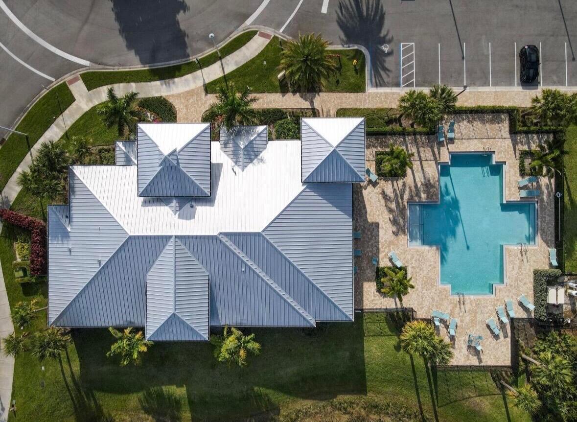 Aerial view of a home with a white metal roof, landscaped yard, and swimming pool.