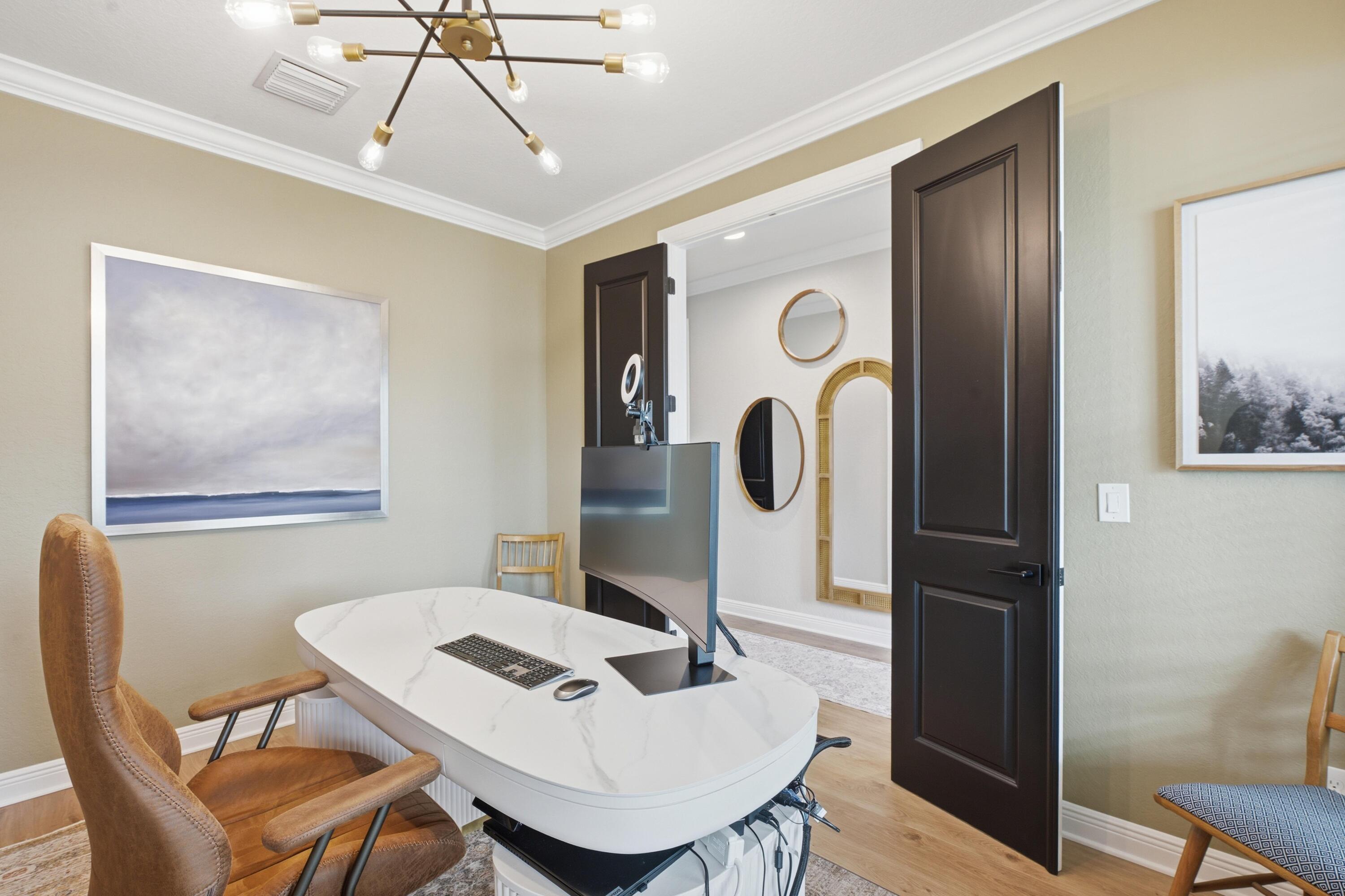 Furnished home office with a marble-look desk, tan leather chair, and open dark double doors.