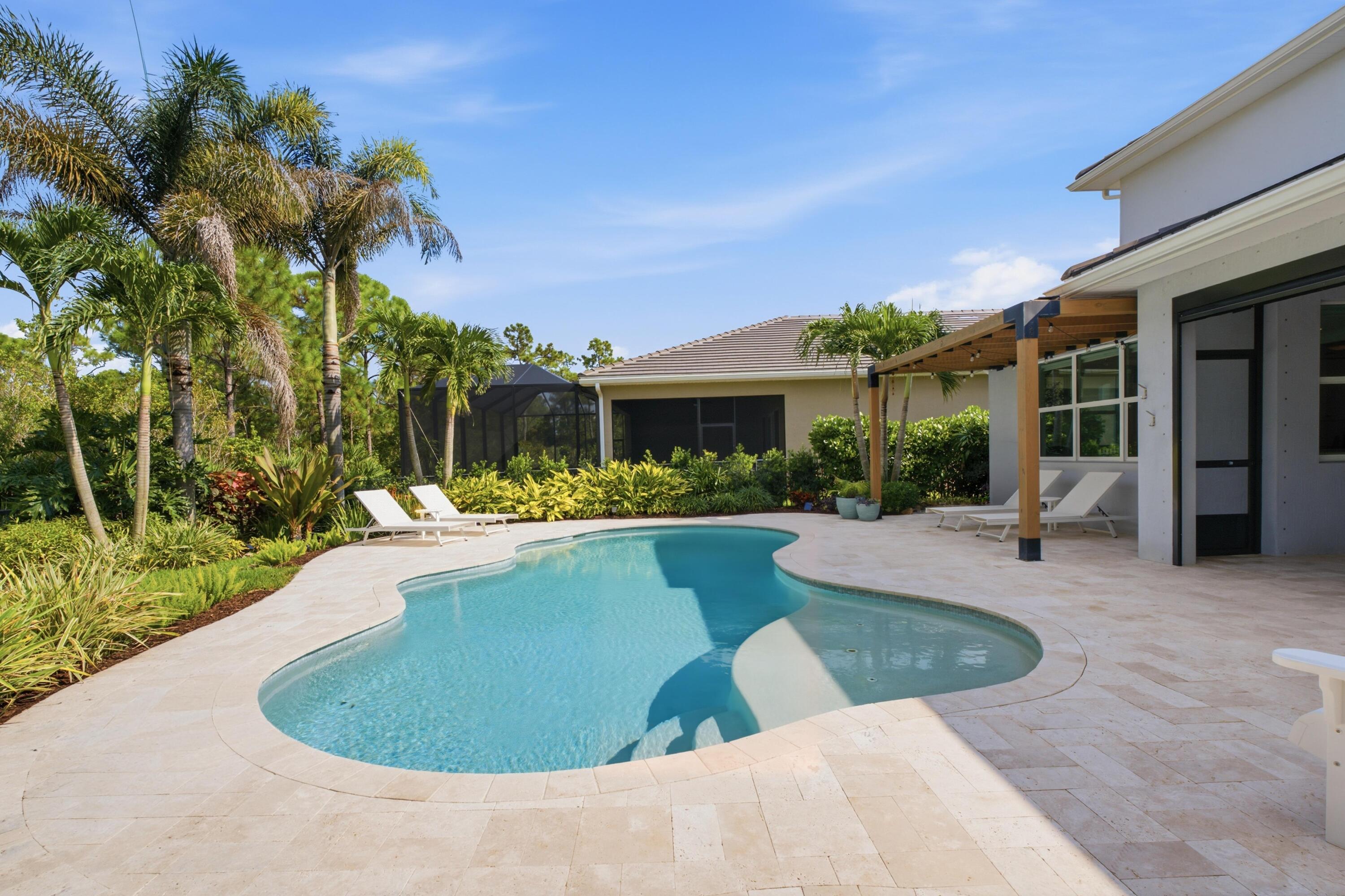 Backyard pool with a curved shape, palm landscaping, and a covered pergola beside the house.