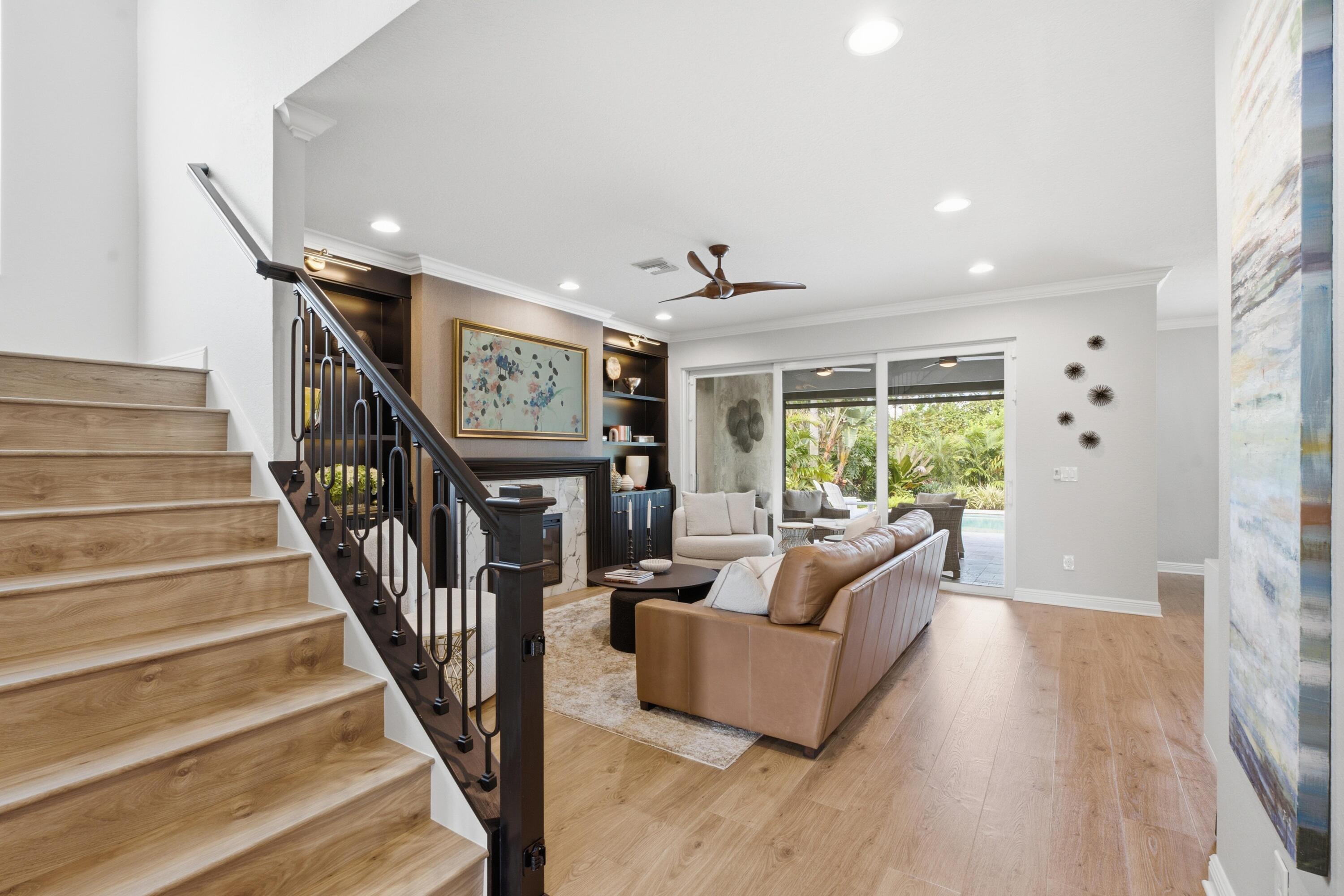 Living room with a wood staircase, fireplace, and sliding doors opening toward a tropical patio.